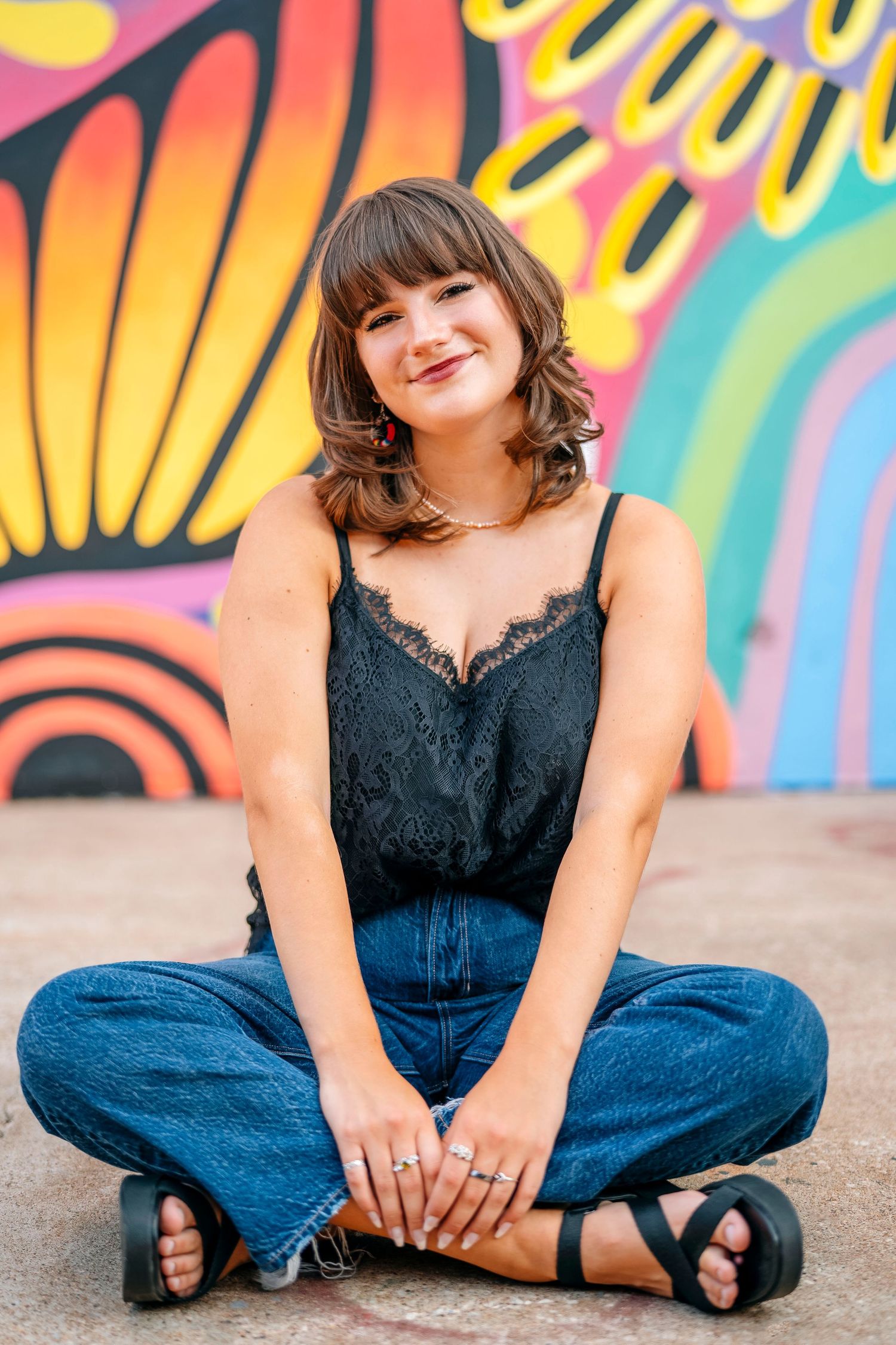 Sitting cross-legged against colorful mural wall in summer casual outfit.