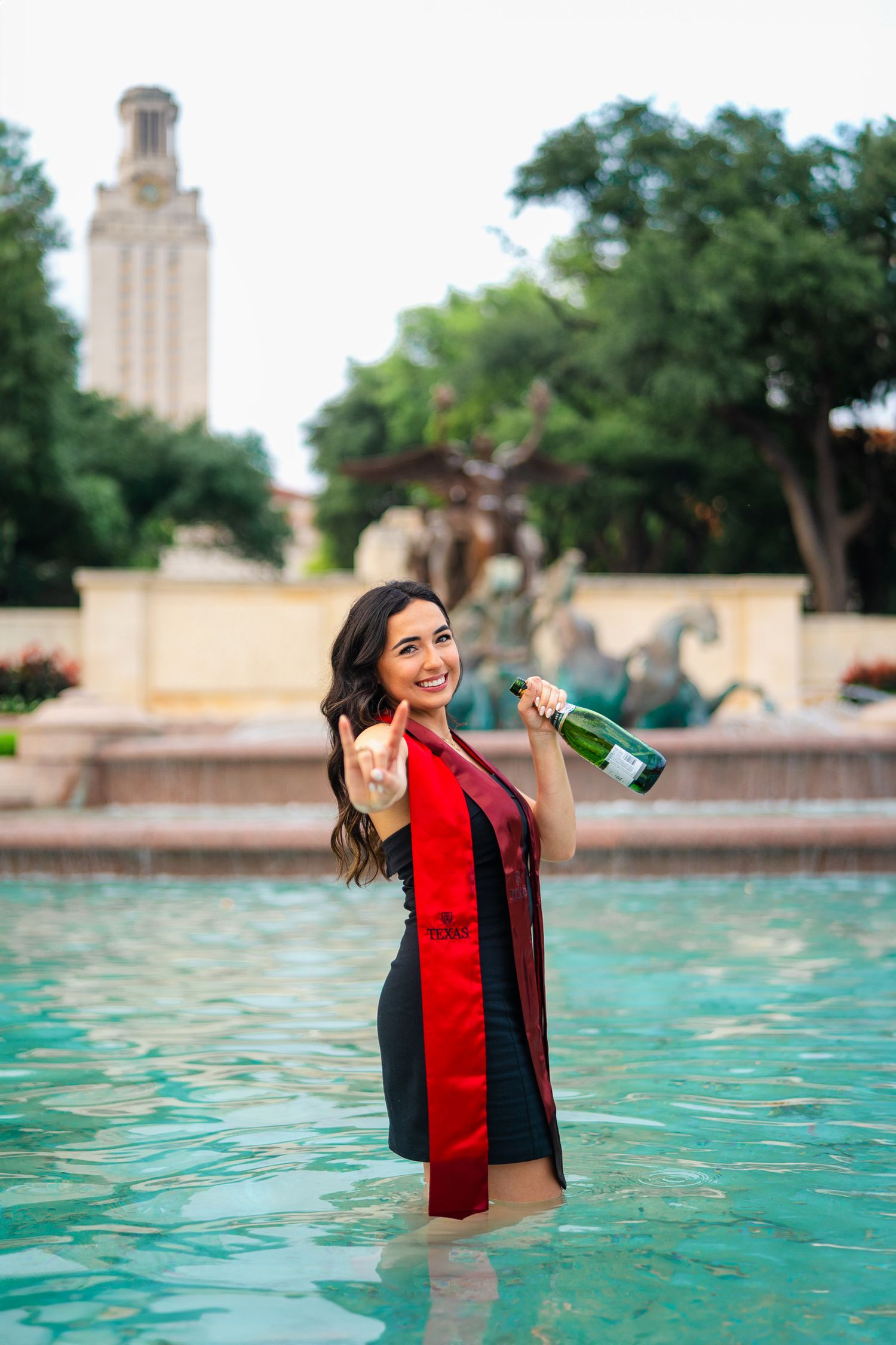 UT senior spraying champagne in cap and gown at Littlefield Fountain