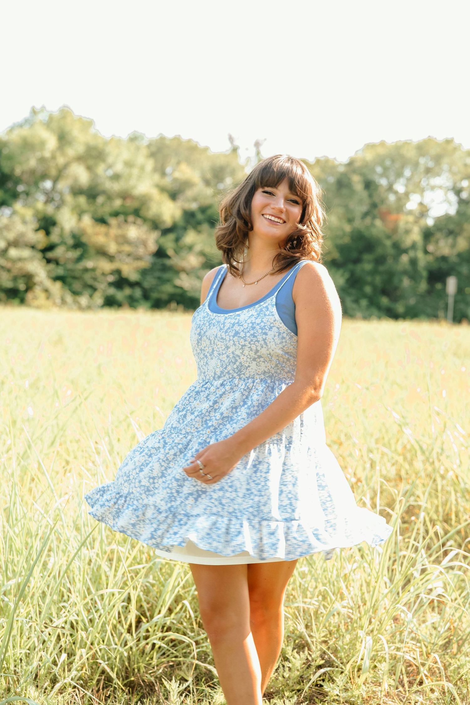 Standing in sunny meadow wearing light blue floral summer dress.