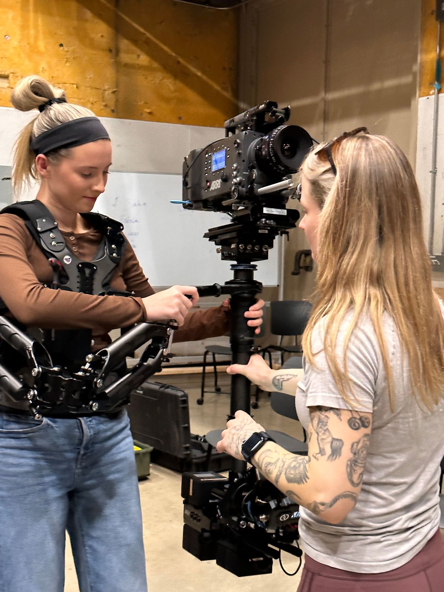 Two crew members work together to adjust a professional camera rig in a studio setting.