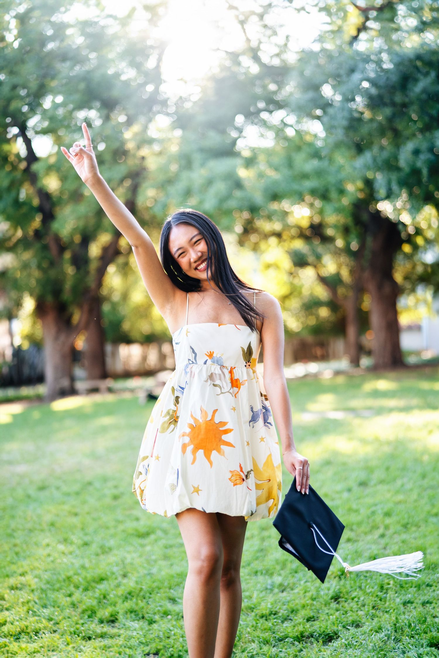 Graduate celebrating with raised arm and cap toss in sunny garden setting.