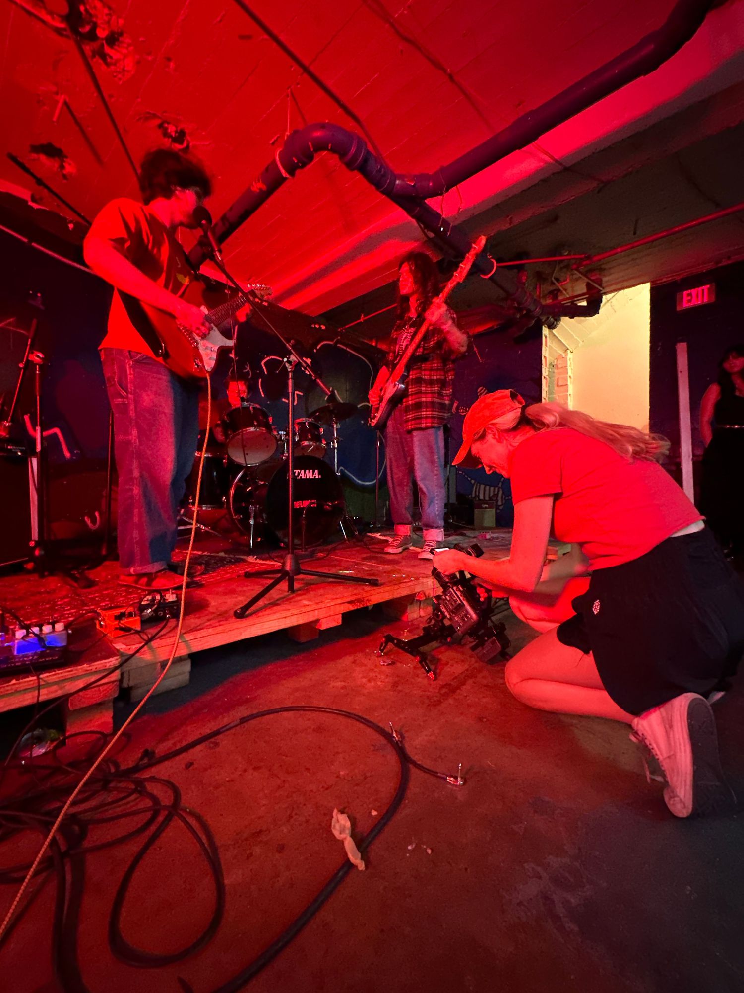 Musicians performing on stage while being filmed under dramatic red lighting.