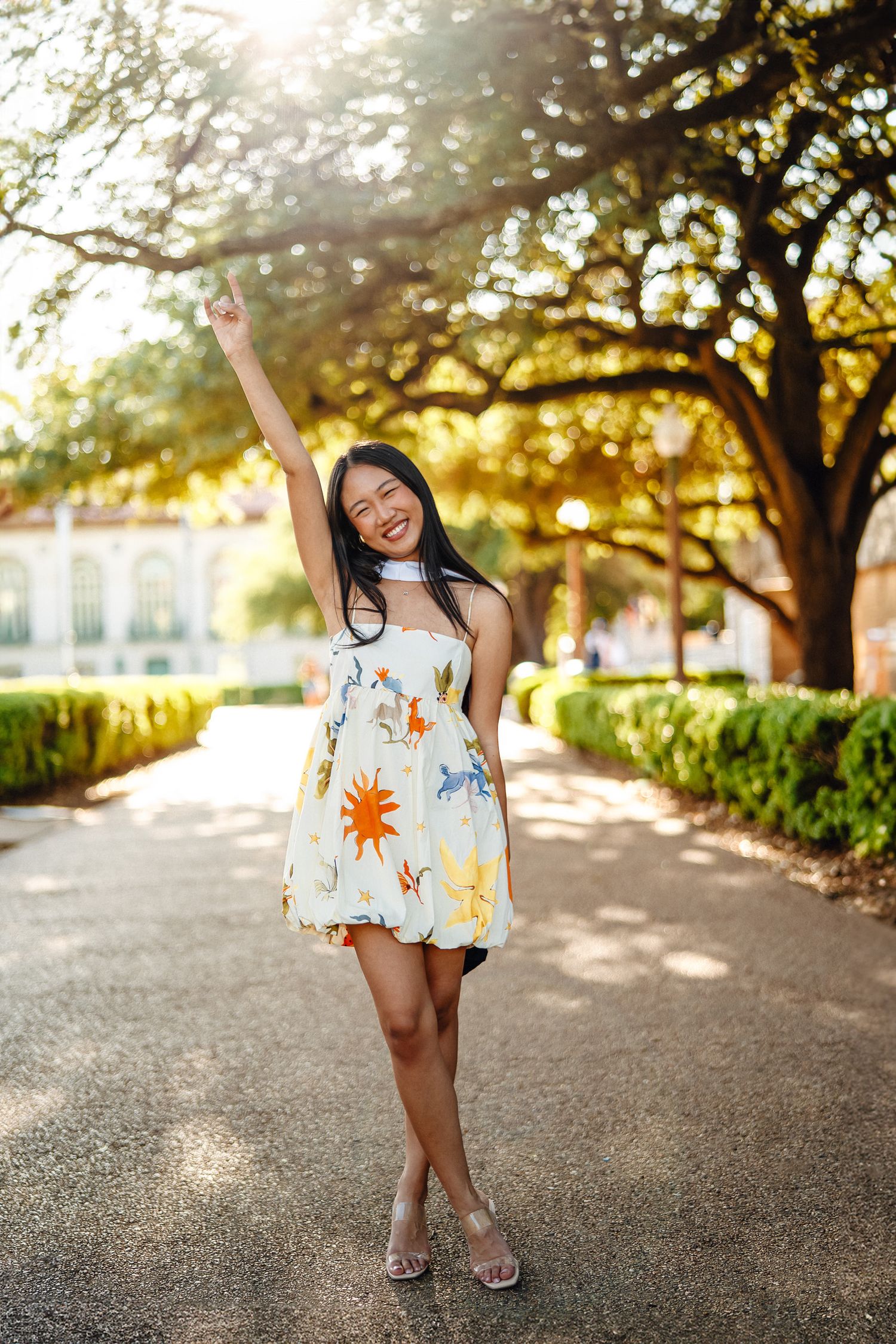 A person in a floral sundress poses cheerfully on a pathway during golden hour.