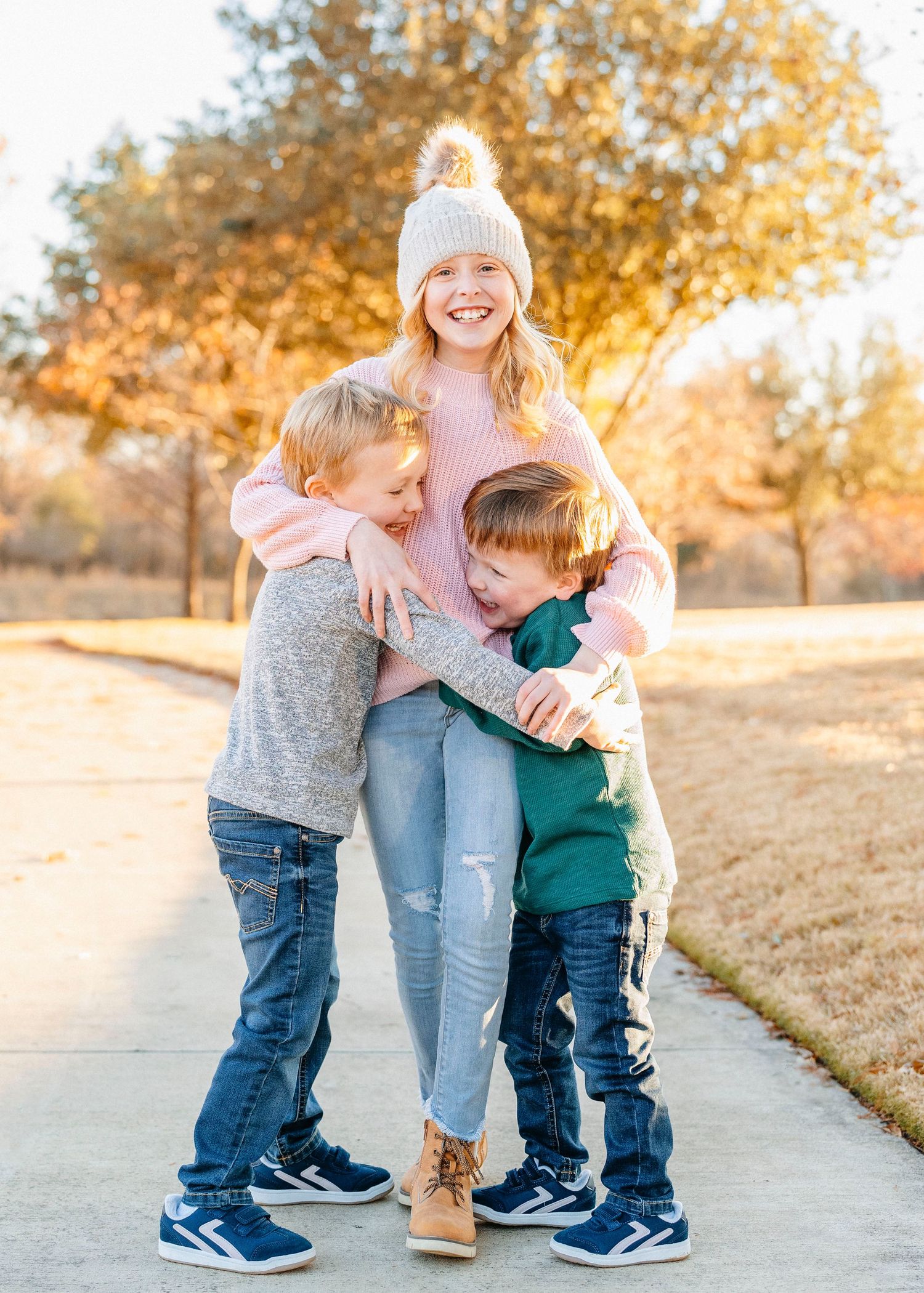 Children hug and play together on walking path during outdoor family photo shoot.