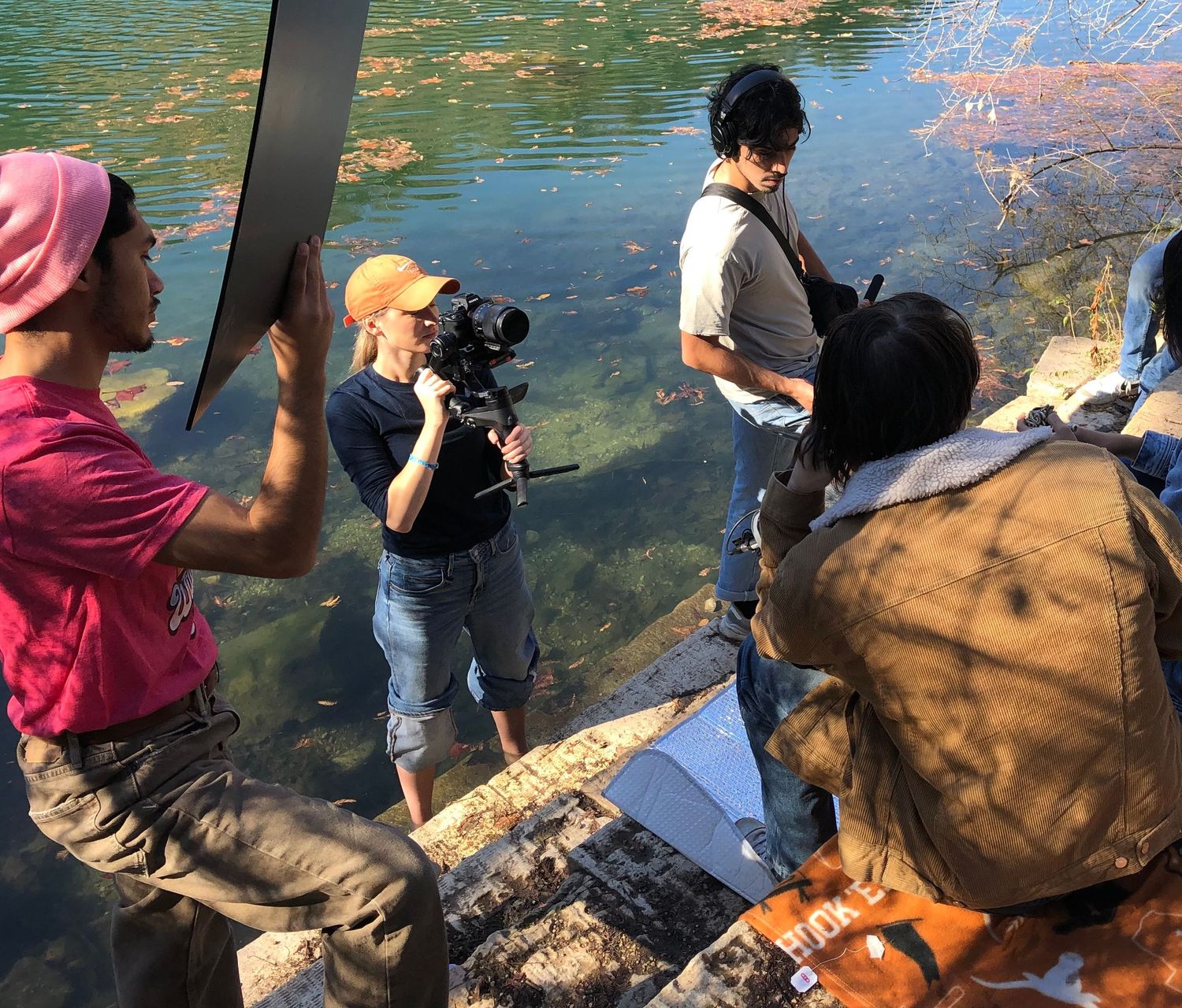 A film crew captures footage near a pond with camera equipment while working outdoors.
