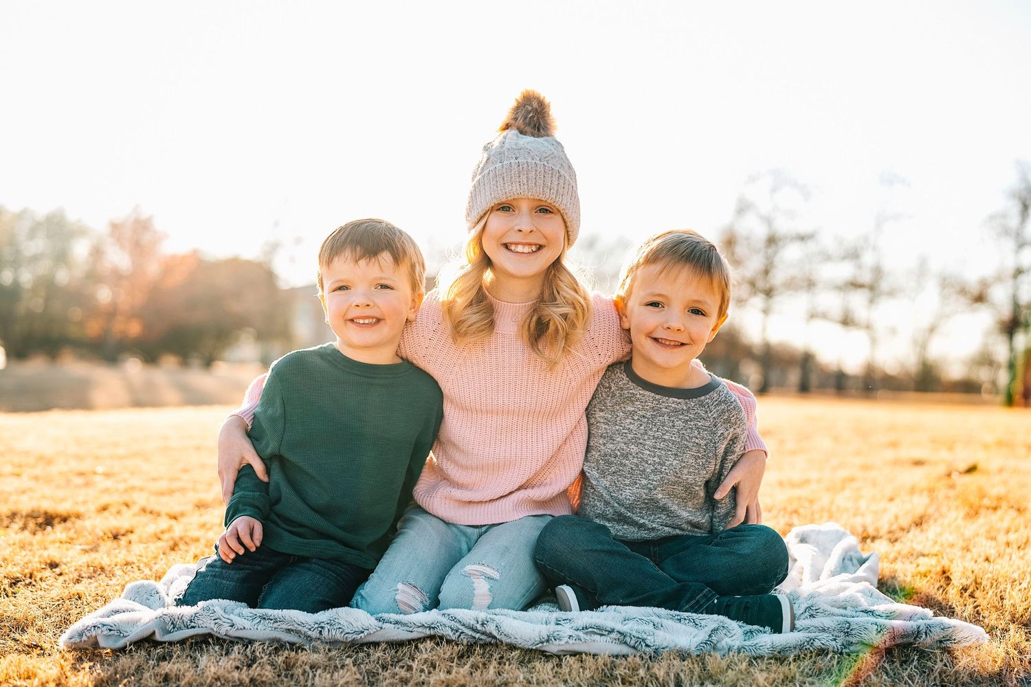 Family photo session on blanket during golden hour in autumn setting.