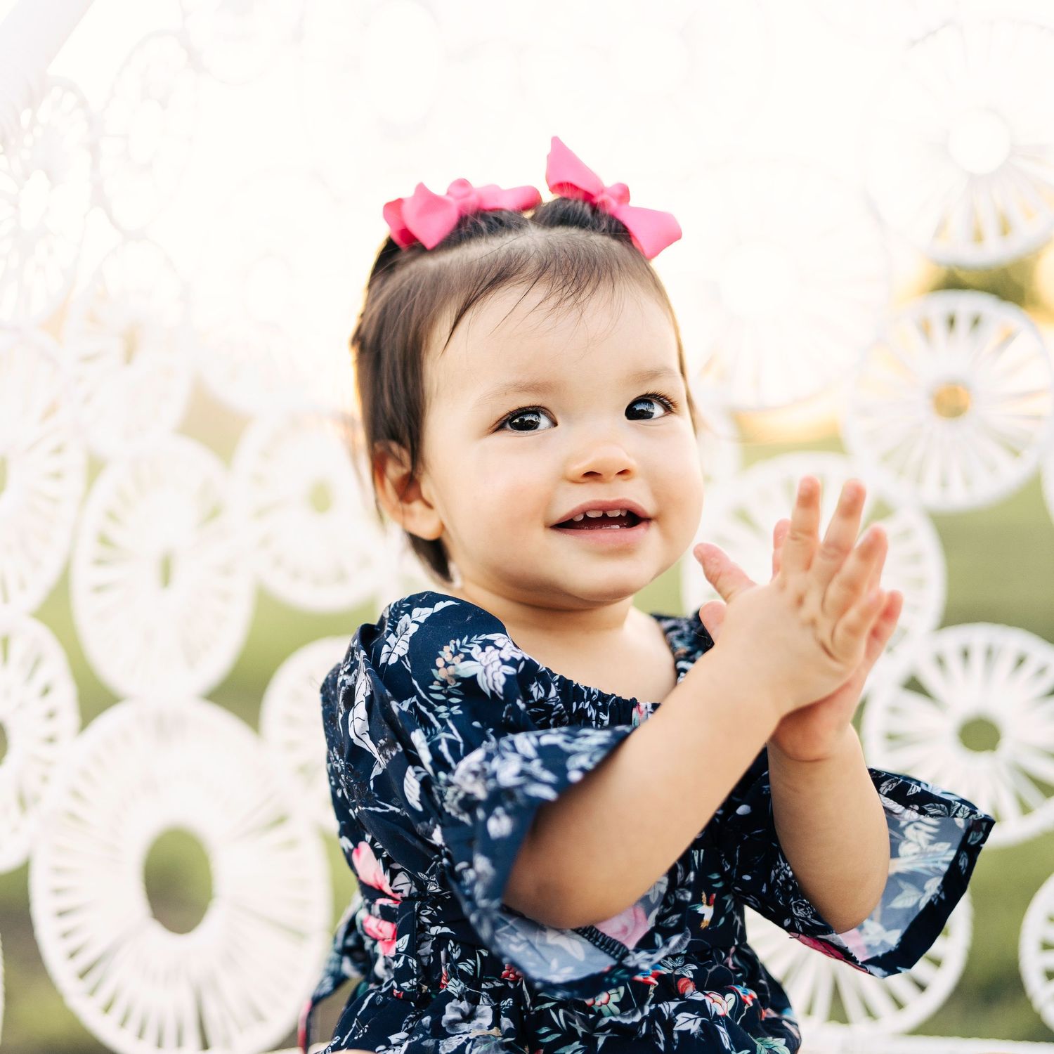 Baby wearing navy floral dress clapping hands with decorative white background.