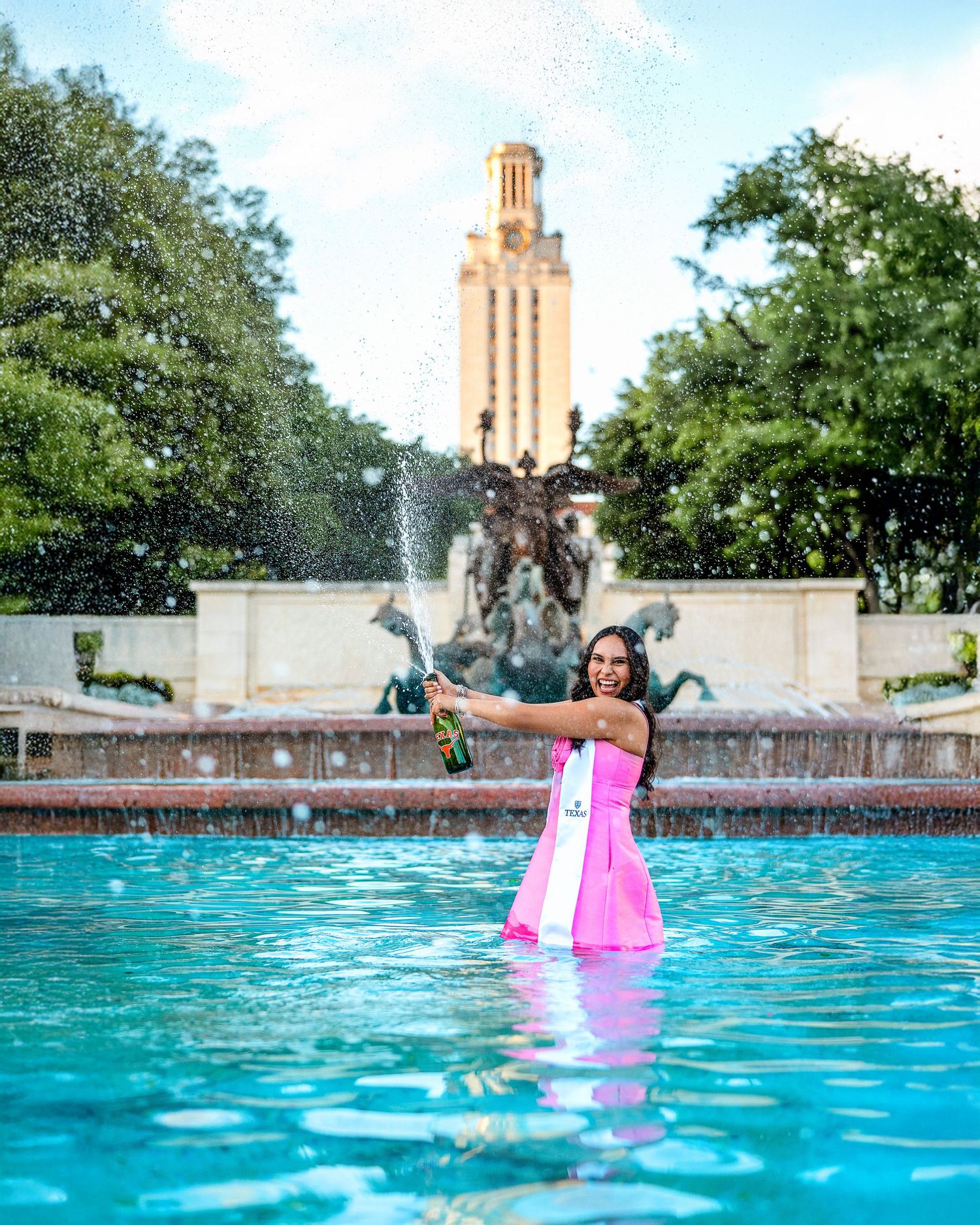 A pink flamingo pool float bobs in bright turquoise water with the iconic UT Austin Tower visible in the background.