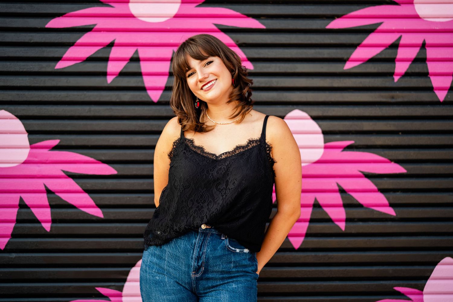 Person posing against black wall with pink neon palm tree decorations.