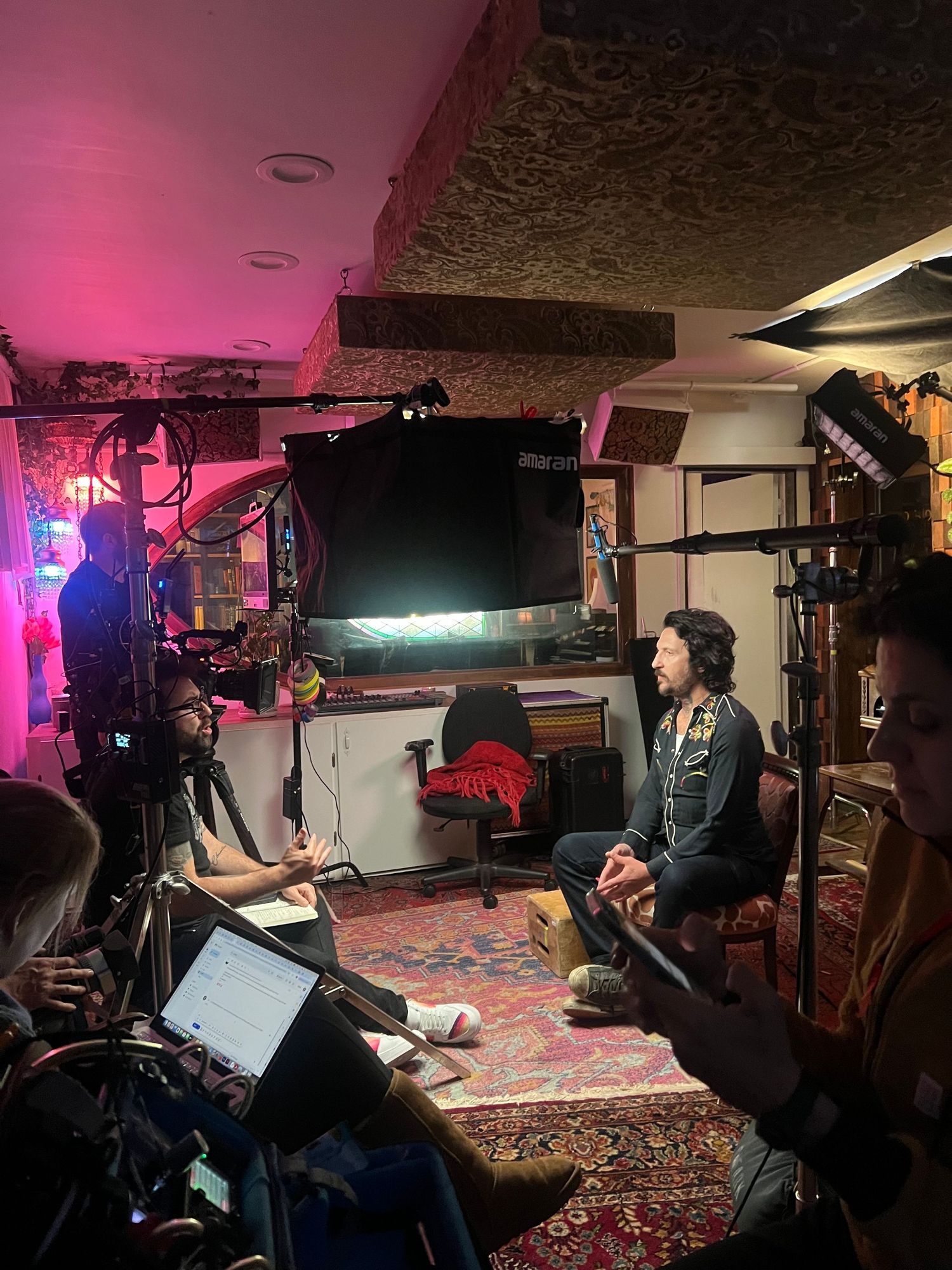 Film crew working in dimly lit room with pink lighting and production equipment.