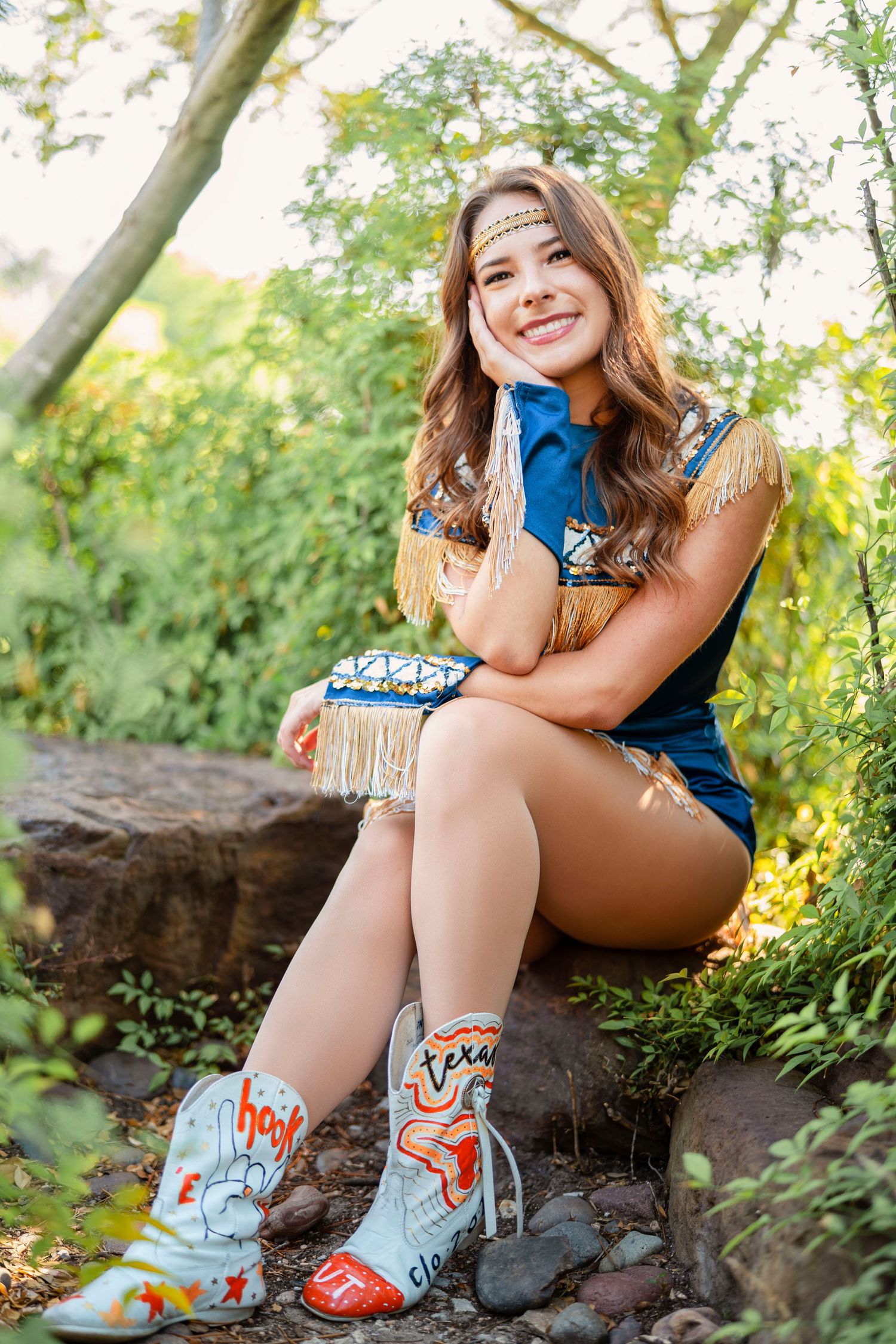 Person in western-style outfit with decorative boots sitting on rock in nature setting.