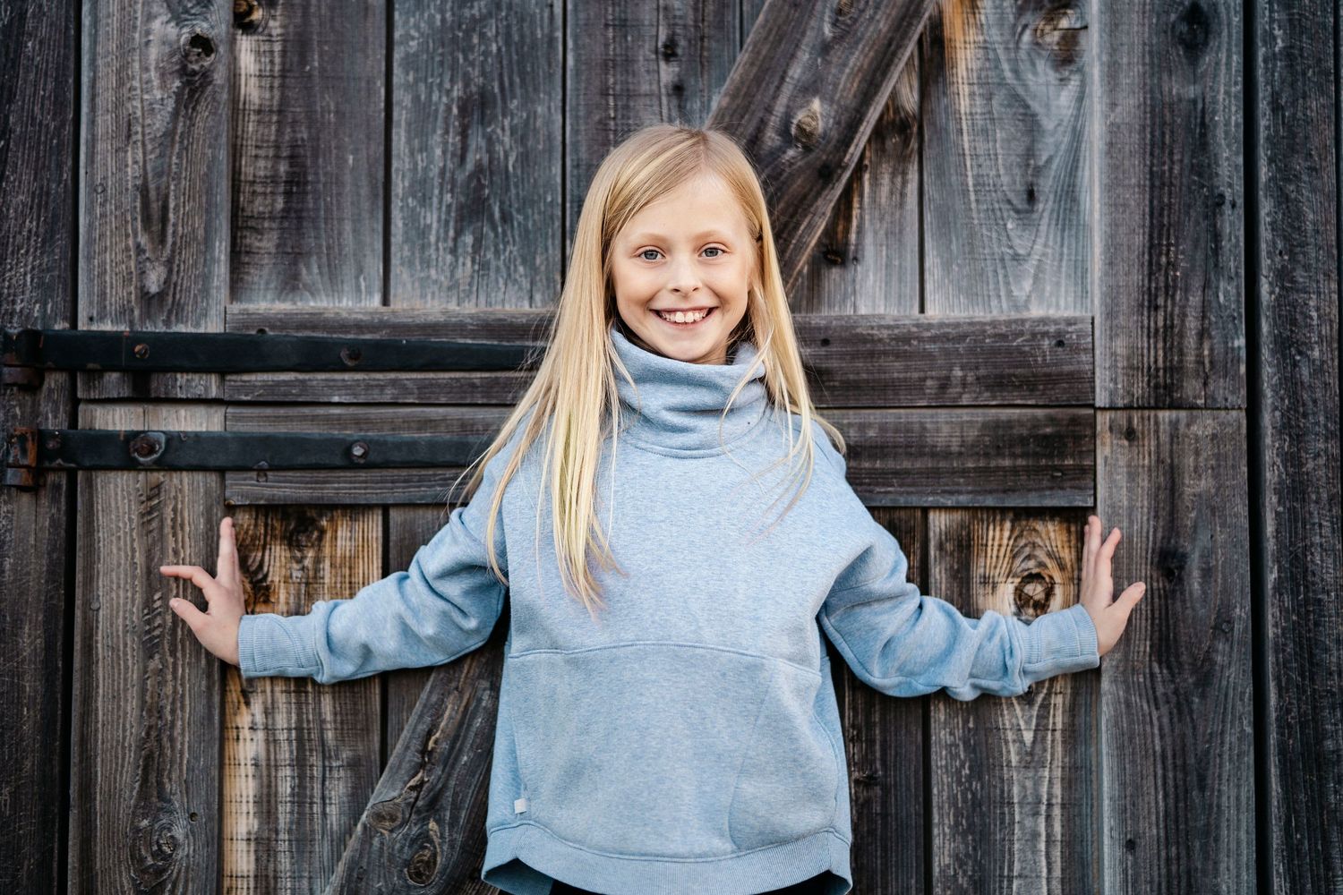Casual poses against rustic barn wood in light blue turtleneck sweater.