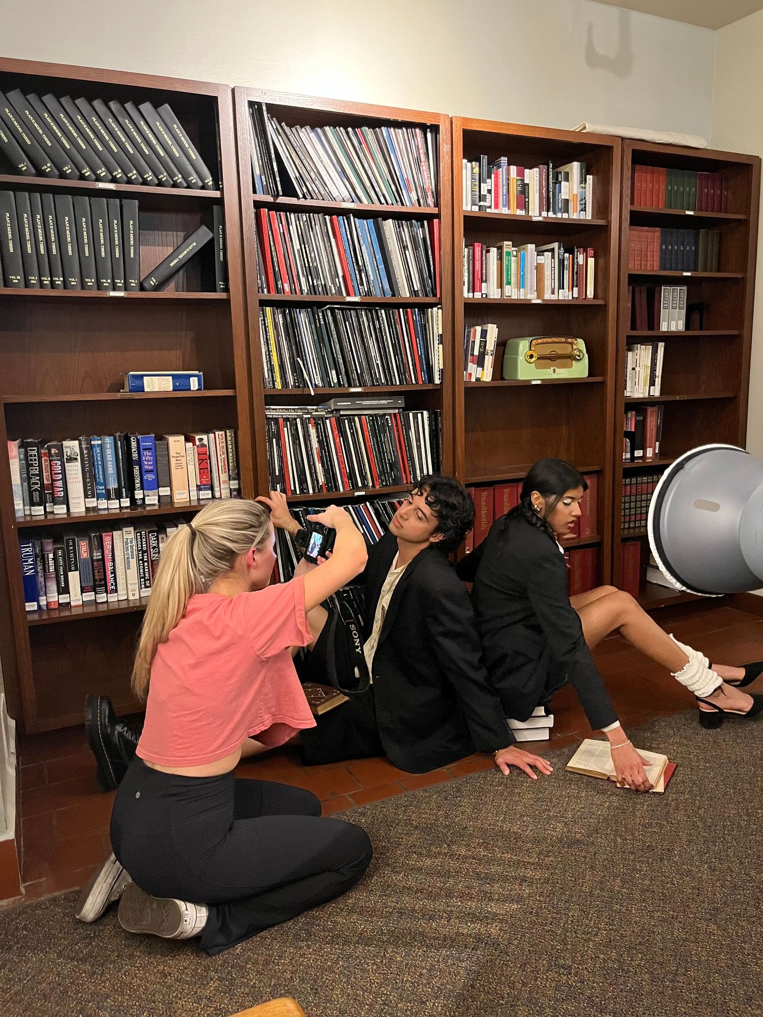 Photography session taking place in library with bookshelves full of media materials.