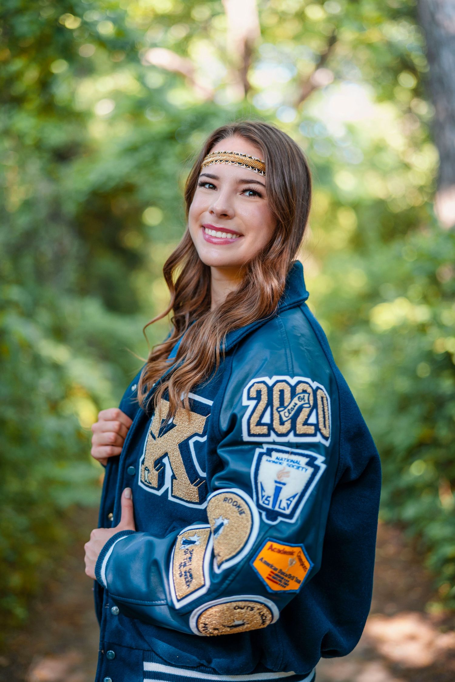 Portrait of someone wearing 2020 varsity letterman jacket with patches in outdoor setting.