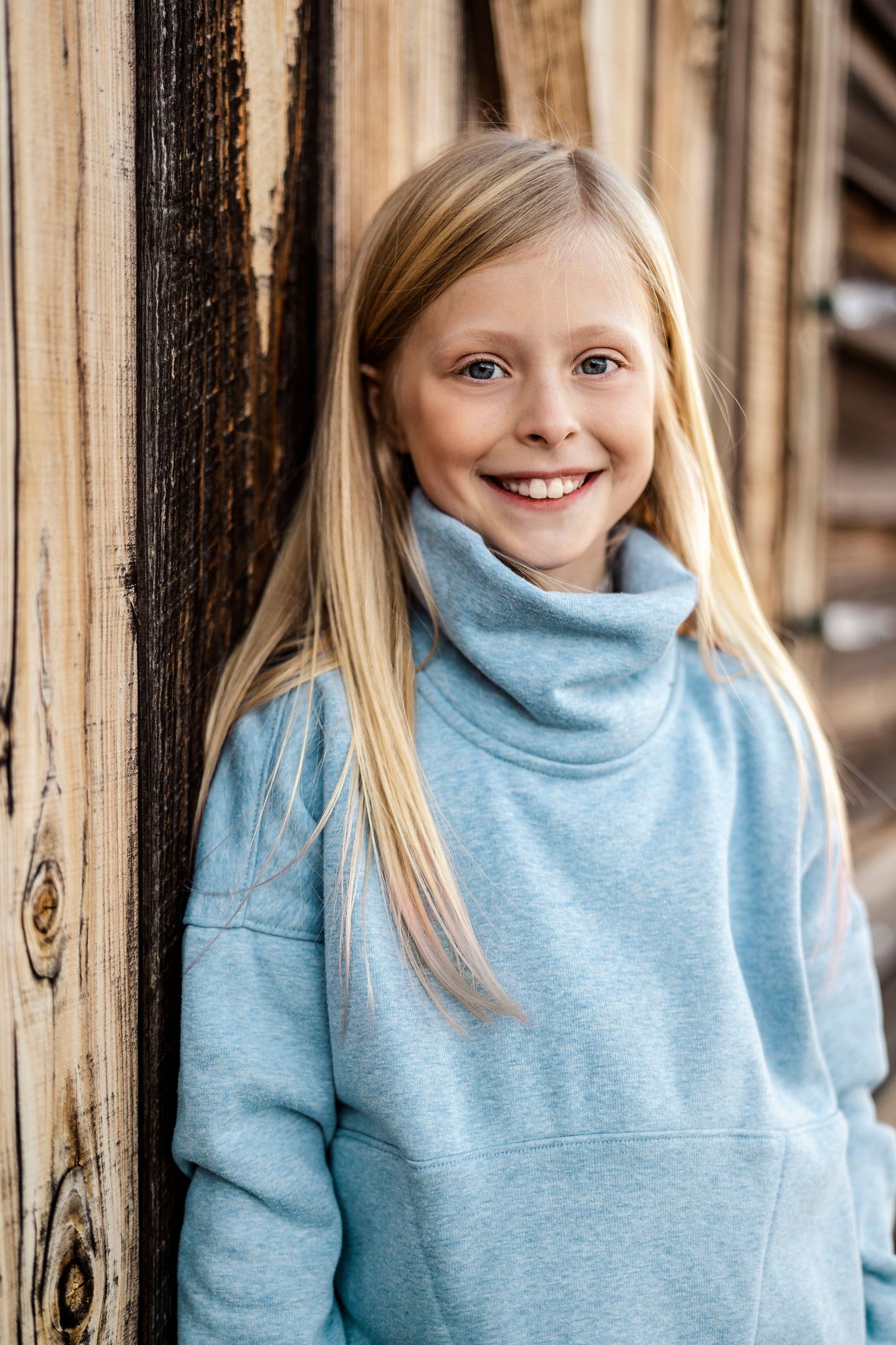 Close-up portrait series in light blue turtleneck against wooden backdrop.