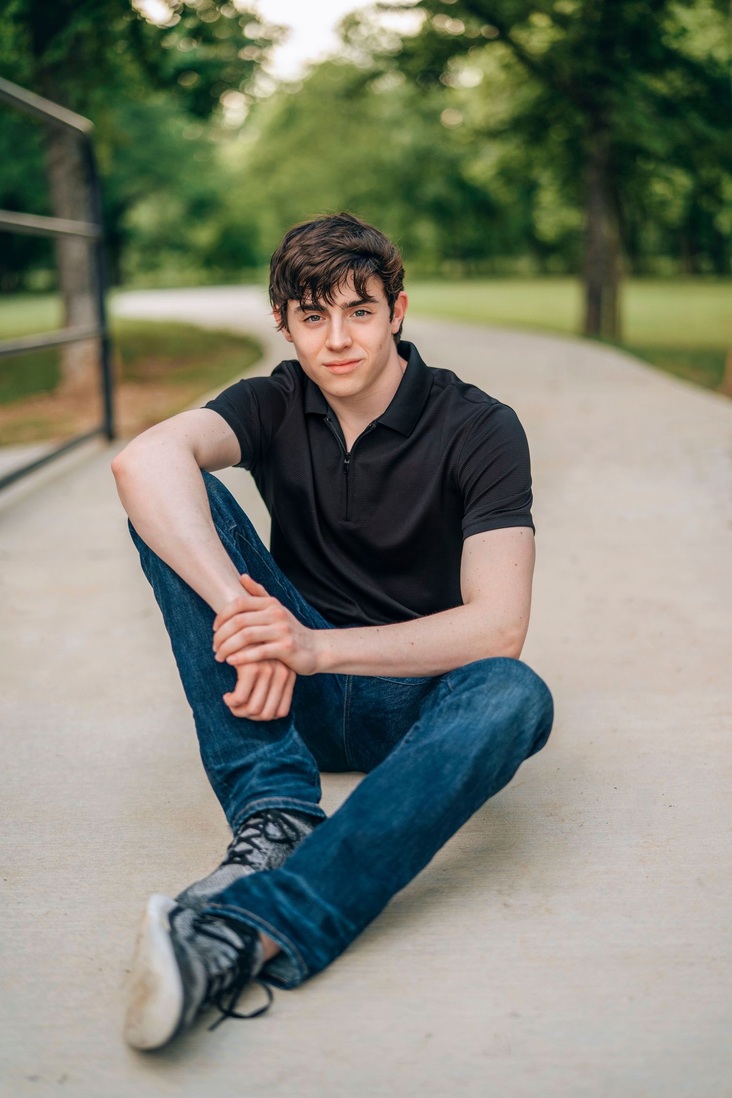 Casual outdoor portrait of someone in black polo shirt sitting on concrete path.