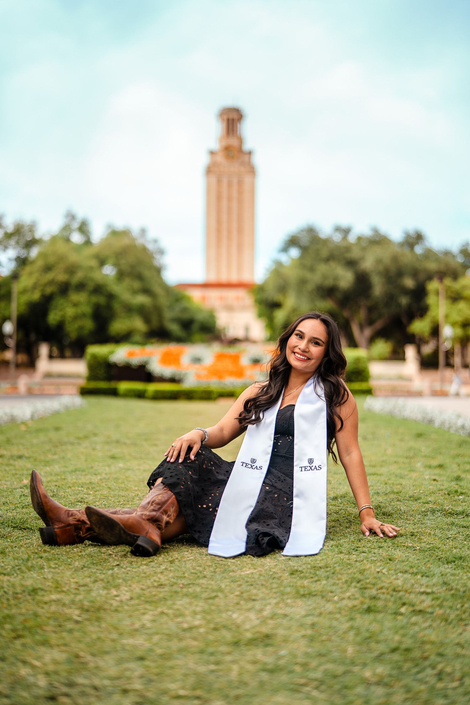 Graduate poses casually on lawn with University of Texas Tower in background.