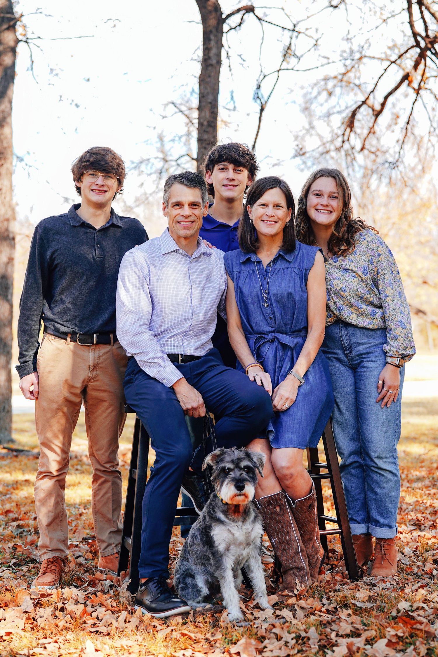 Family portrait with parents and children sitting together with their dog in a fall outdoor setting.