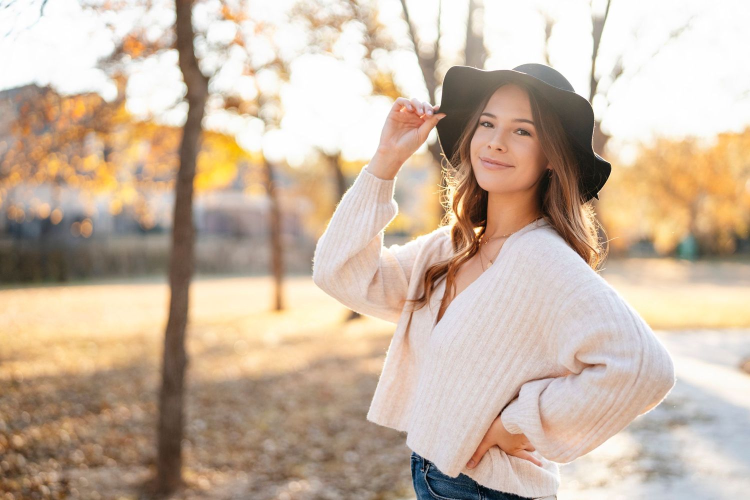 Stylish portrait of someone in white sweater and black hat posing in autumn park setting.