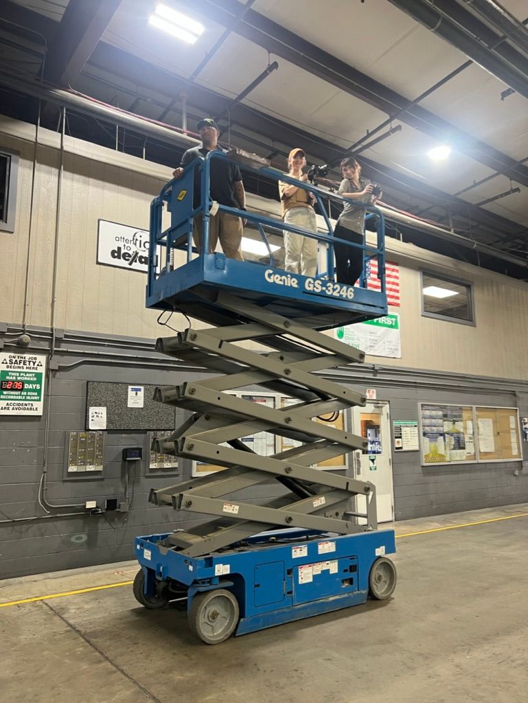 Workers standing on elevated scissor lift platform in industrial warehouse setting.