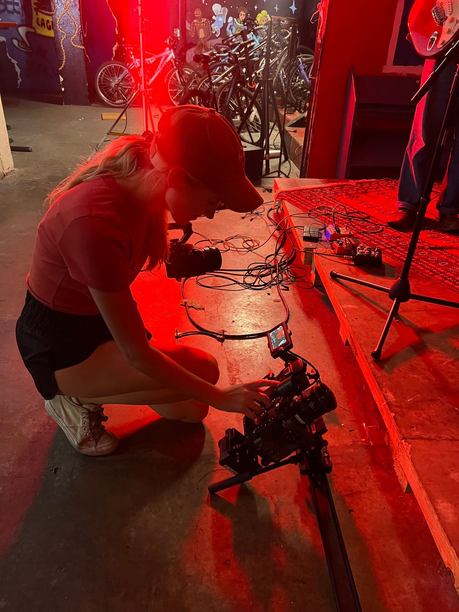 A technician adjusts equipment in a dark venue lit by red theatrical lighting.