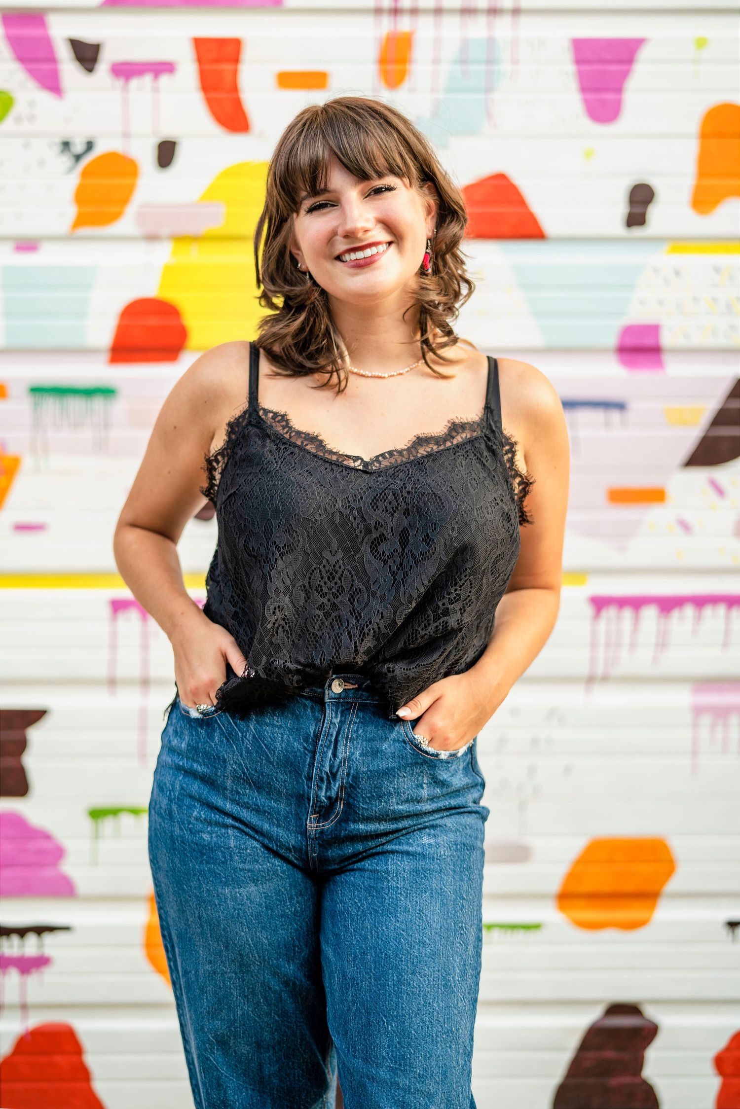 Colorful urban photoshoot against a vibrant mural wall wearing black top and blue jeans.