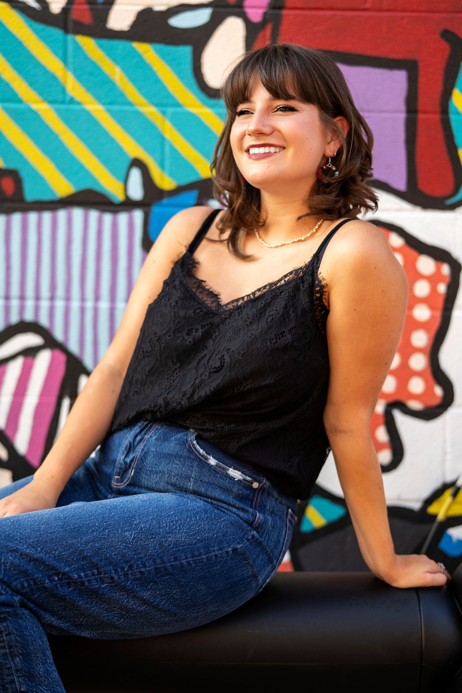Casual portrait against vibrant street art wall wearing black tank top and jeans.