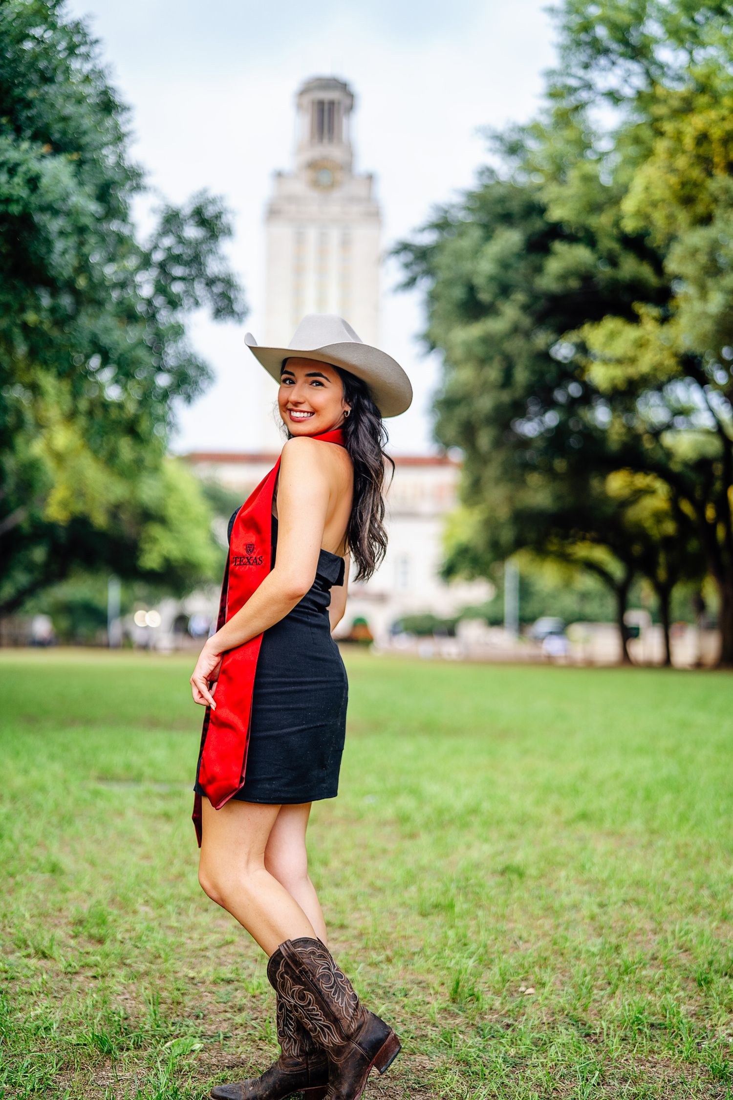 Graduate wearing cowboy boots and hat poses playfully in front of iconic UT Tower.