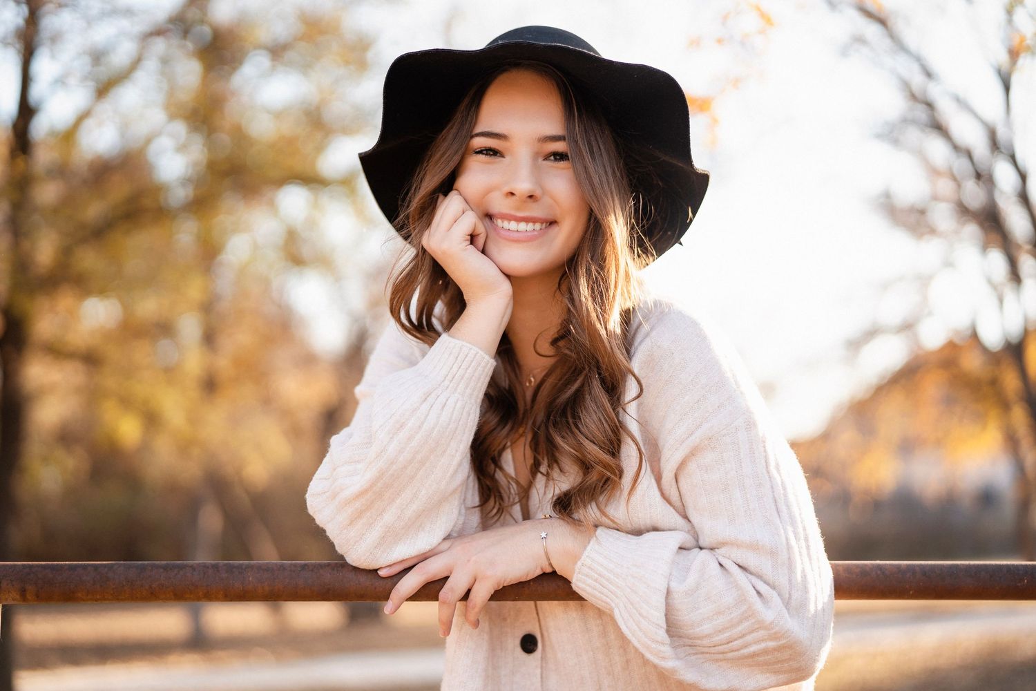 Outdoor portrait of someone wearing a cream sweater and black hat in warm autumn lighting.