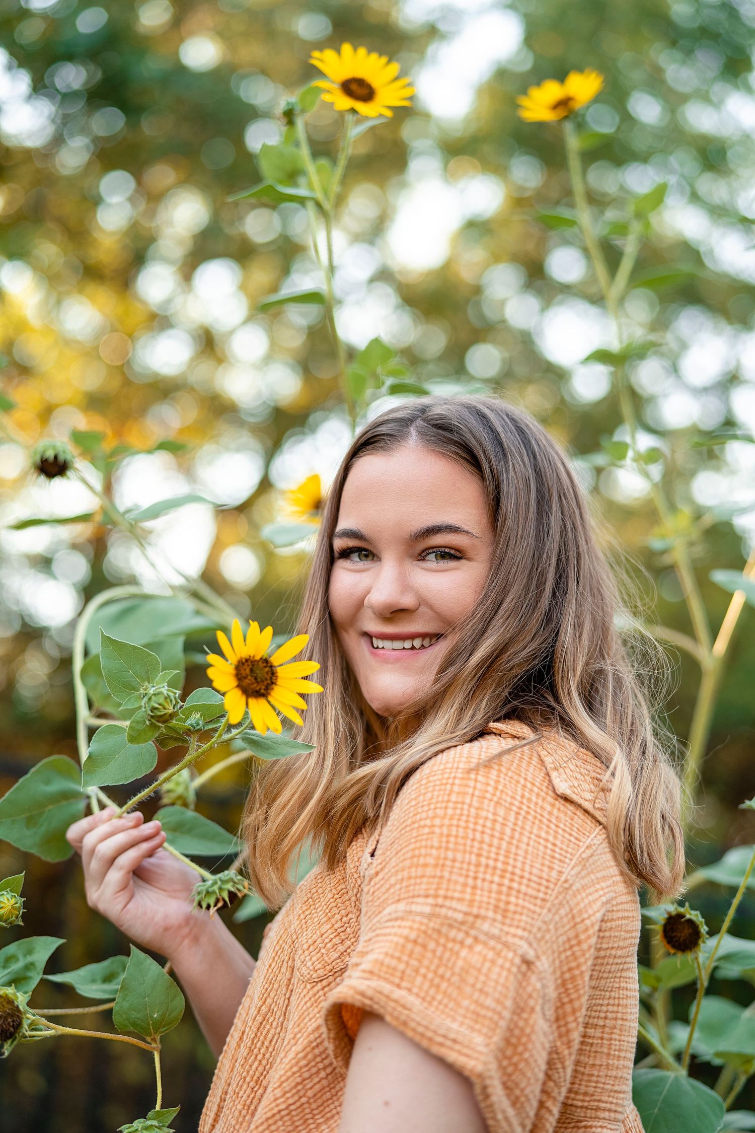 A joyful portrait among blooming sunflowers wearing a peach-colored top.