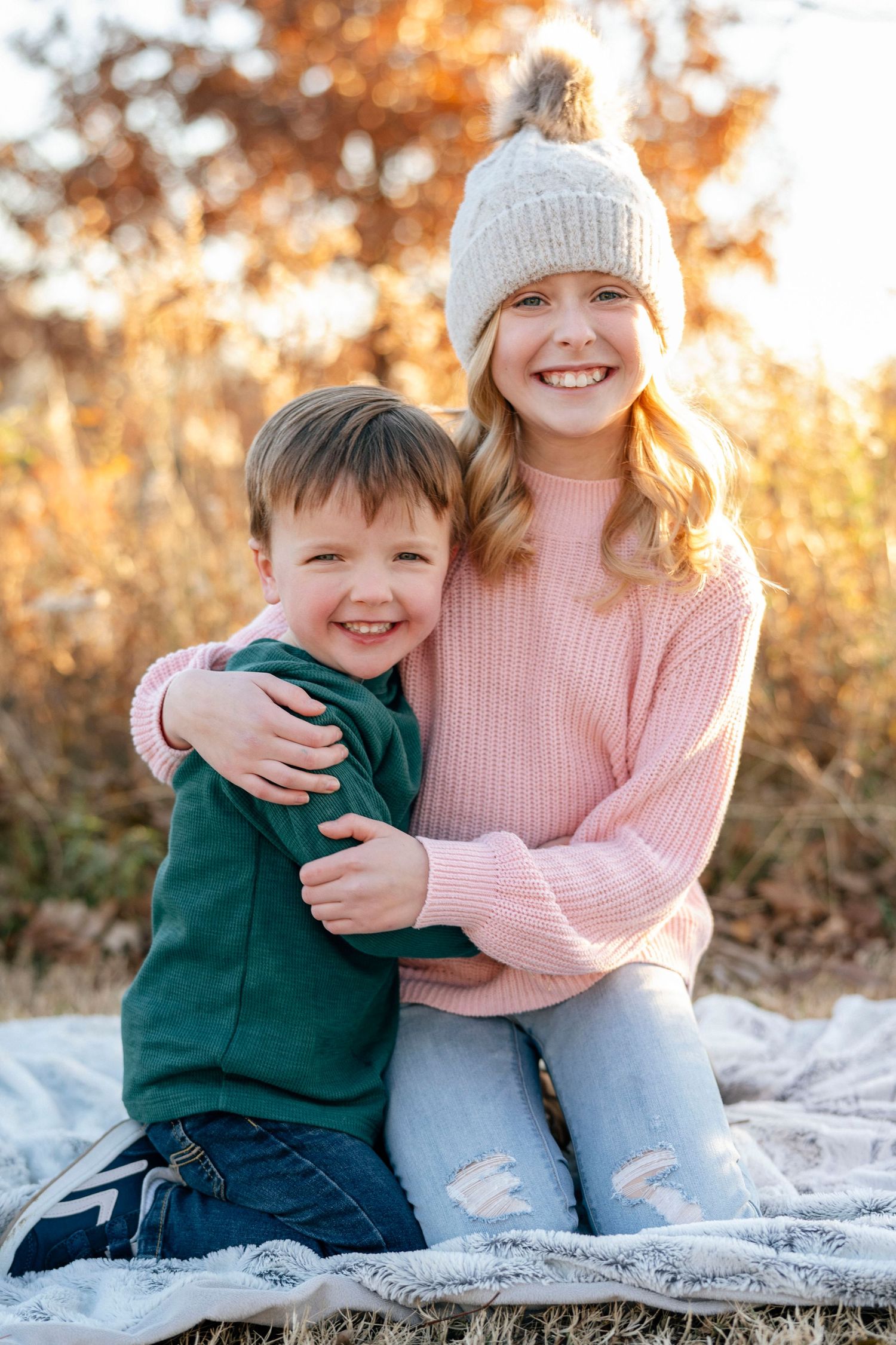 Two people sitting on blanket outdoors sharing warm embrace during autumn photoshoot.