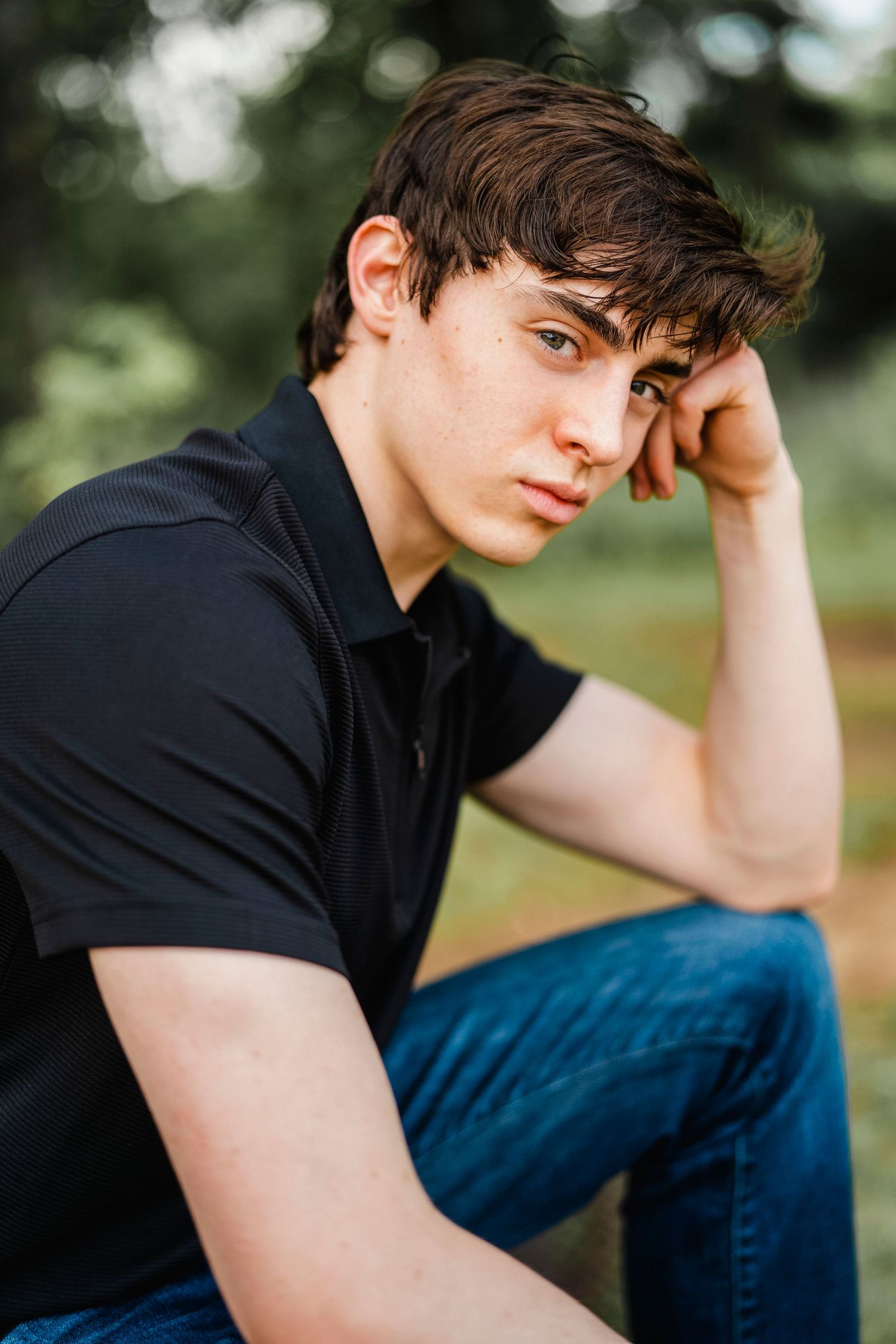 A casual outdoor portrait against blurred trees wearing a black t-shirt and jeans.