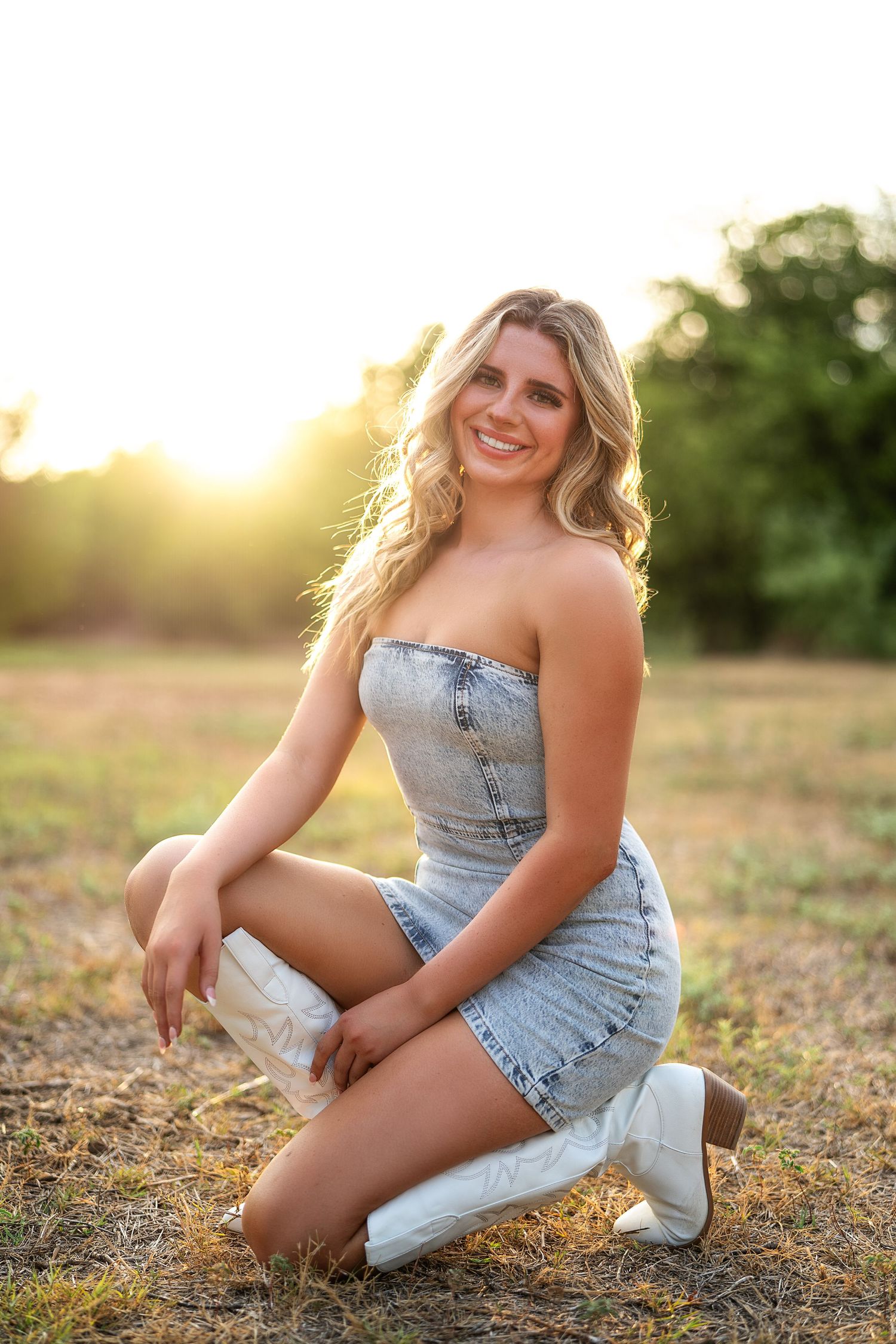 Person sitting on ground wearing denim and white sneakers in warm sunset lighting.