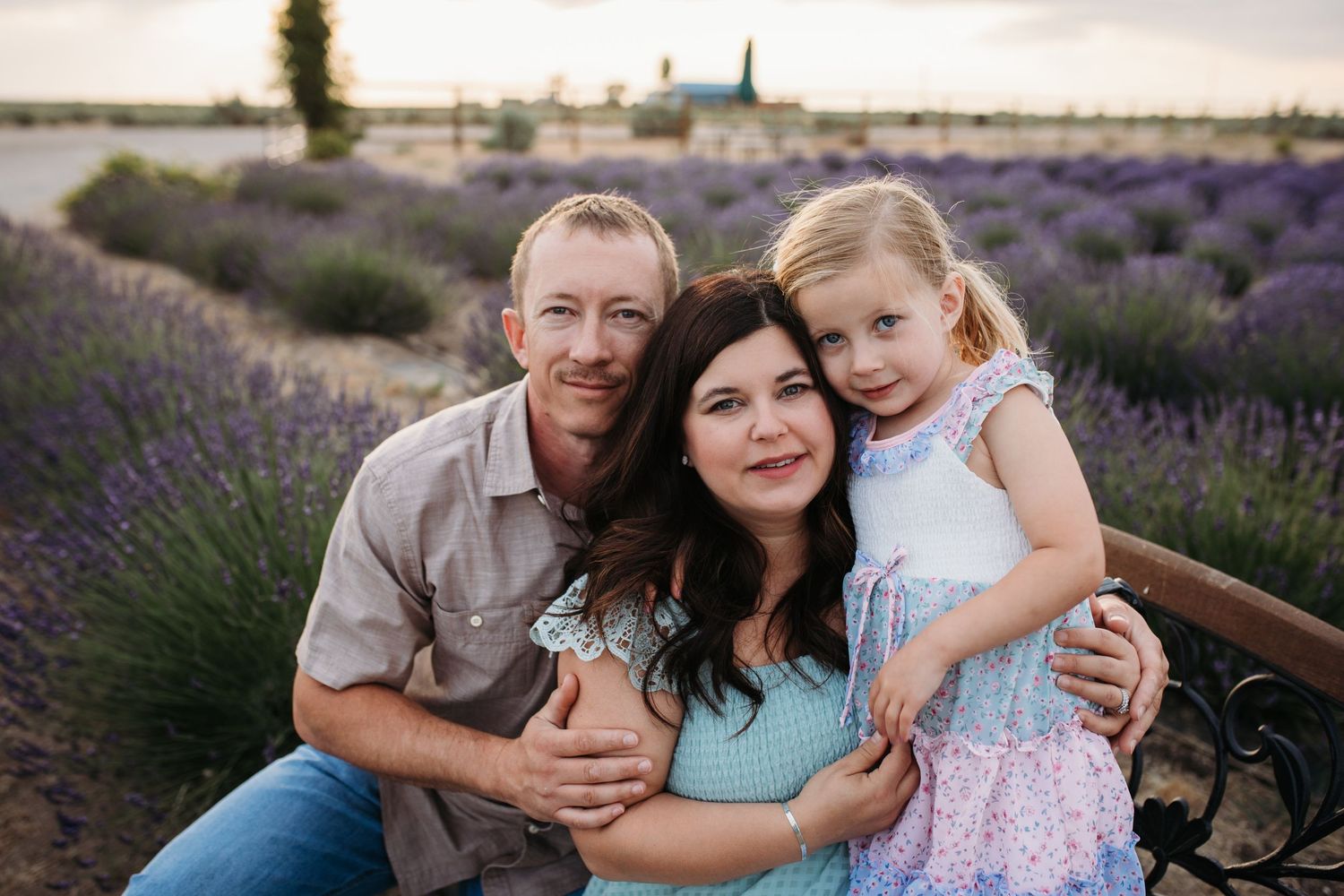 Family embracing on a bench surrounded by blooming lavender during a summer photography session in Idaho.