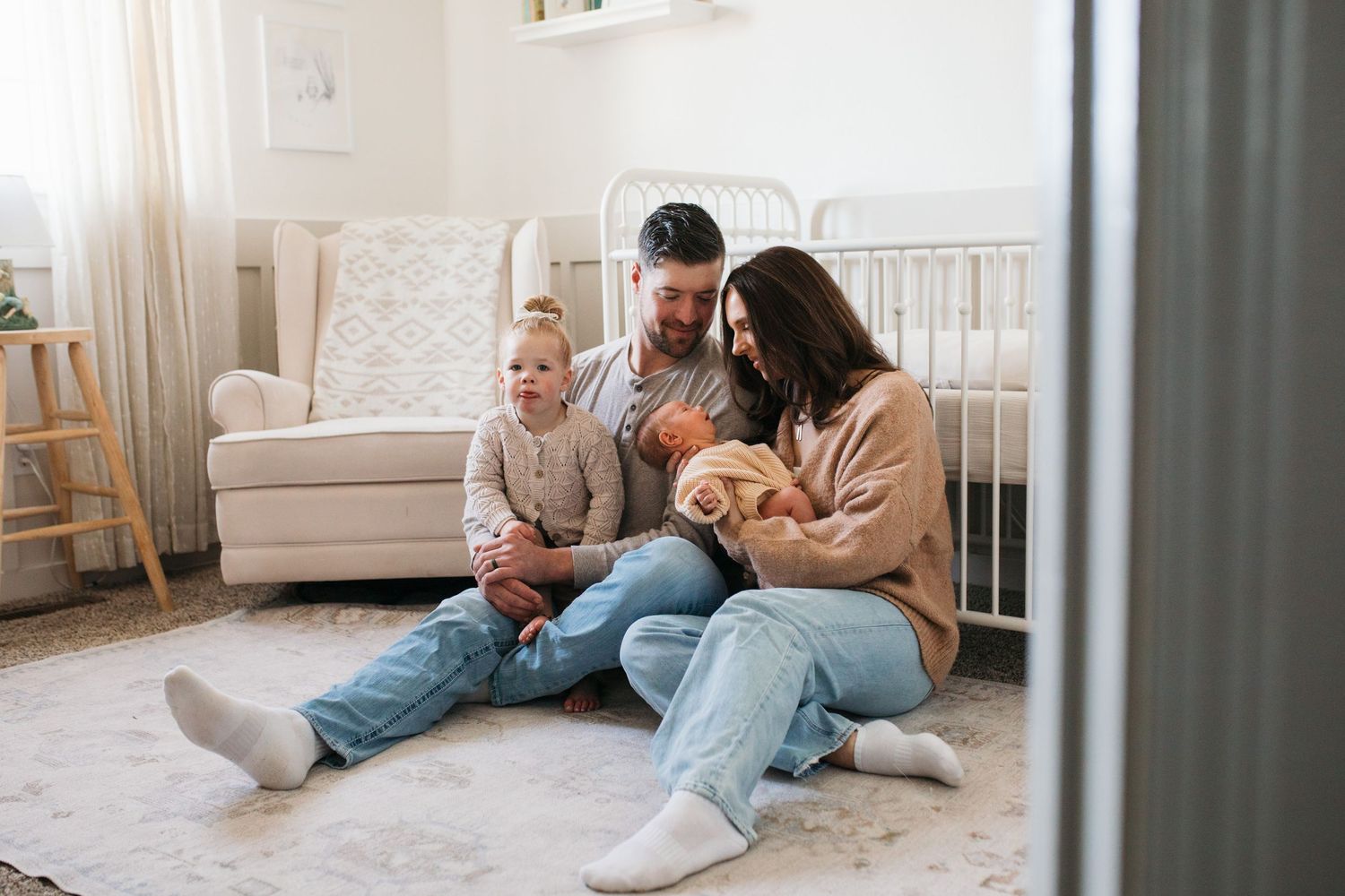 Lifestyle newborn session in Boise with parents and toddler sitting in nursery holding their newborn baby