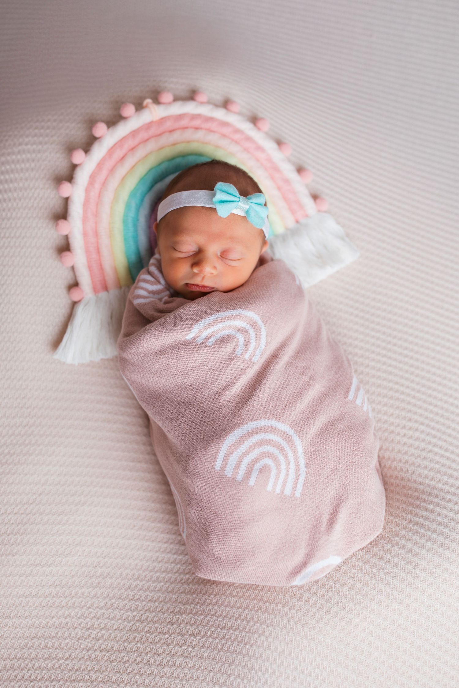 Newborn baby girl wrapped in a pink rainbow blanket posed beneath a pastel rainbow during a Nampa studio newborn session.