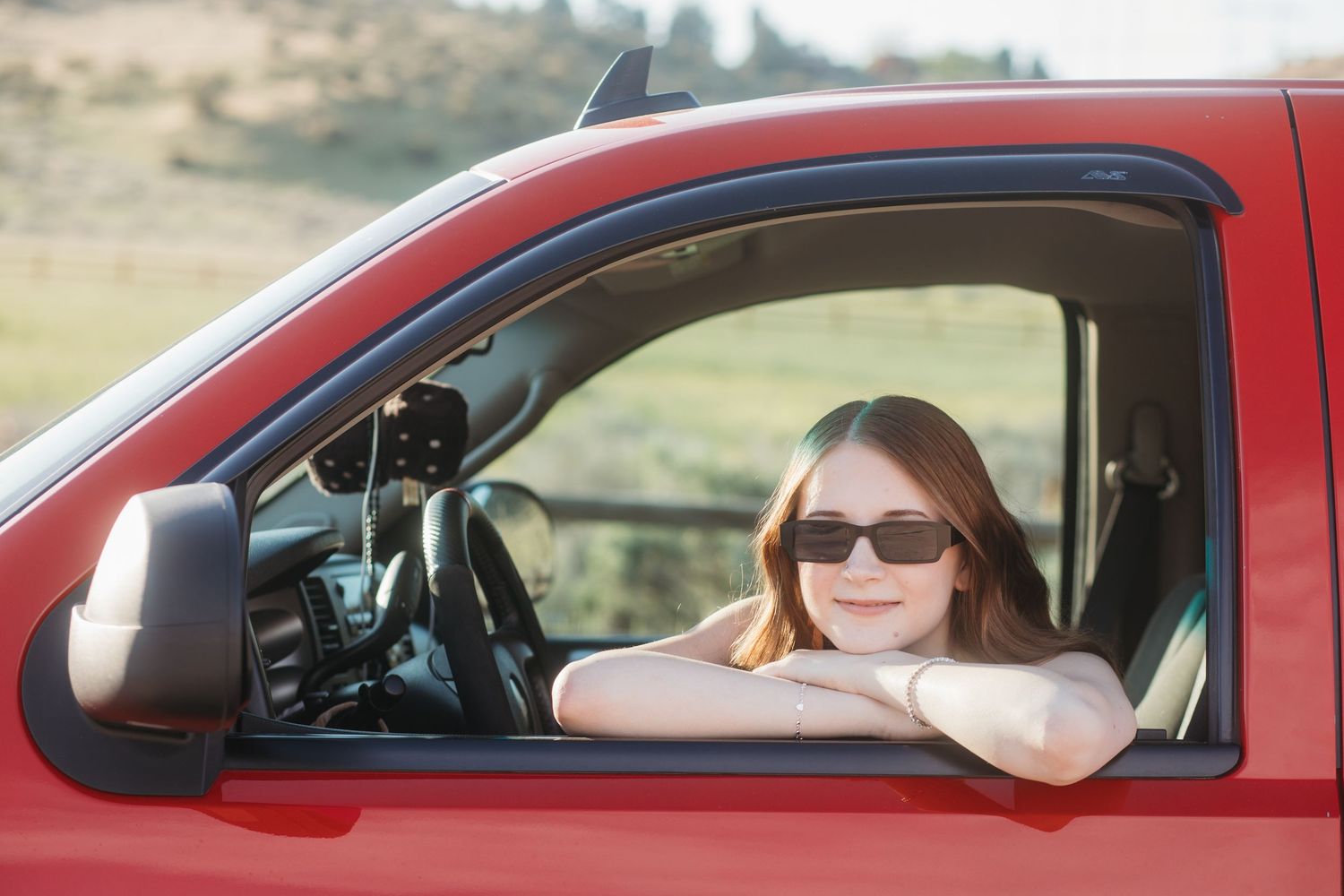 Boise senior photos of high school girl wearing sunglasses sitting in red truck during outdoor golden hour session