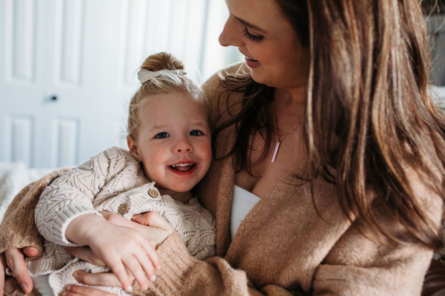 A tender moment between parent and child wearing cozy beige sweaters as they share laughter together -in-home lifestyle family photos Boise