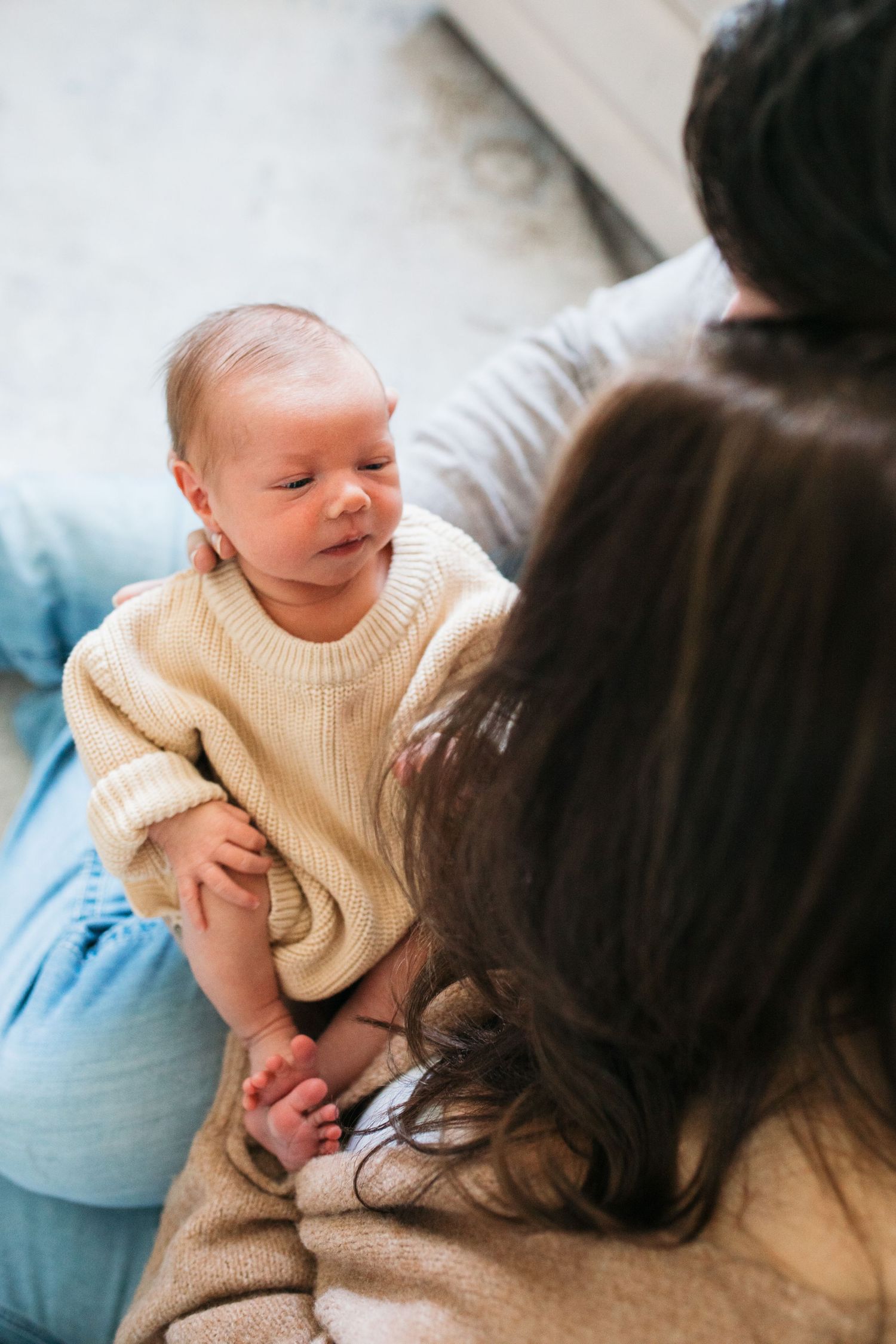 A baby wearing a cream sweater, being held during an intimate indoor photo session - lifestyle in-home newborn photos Boise