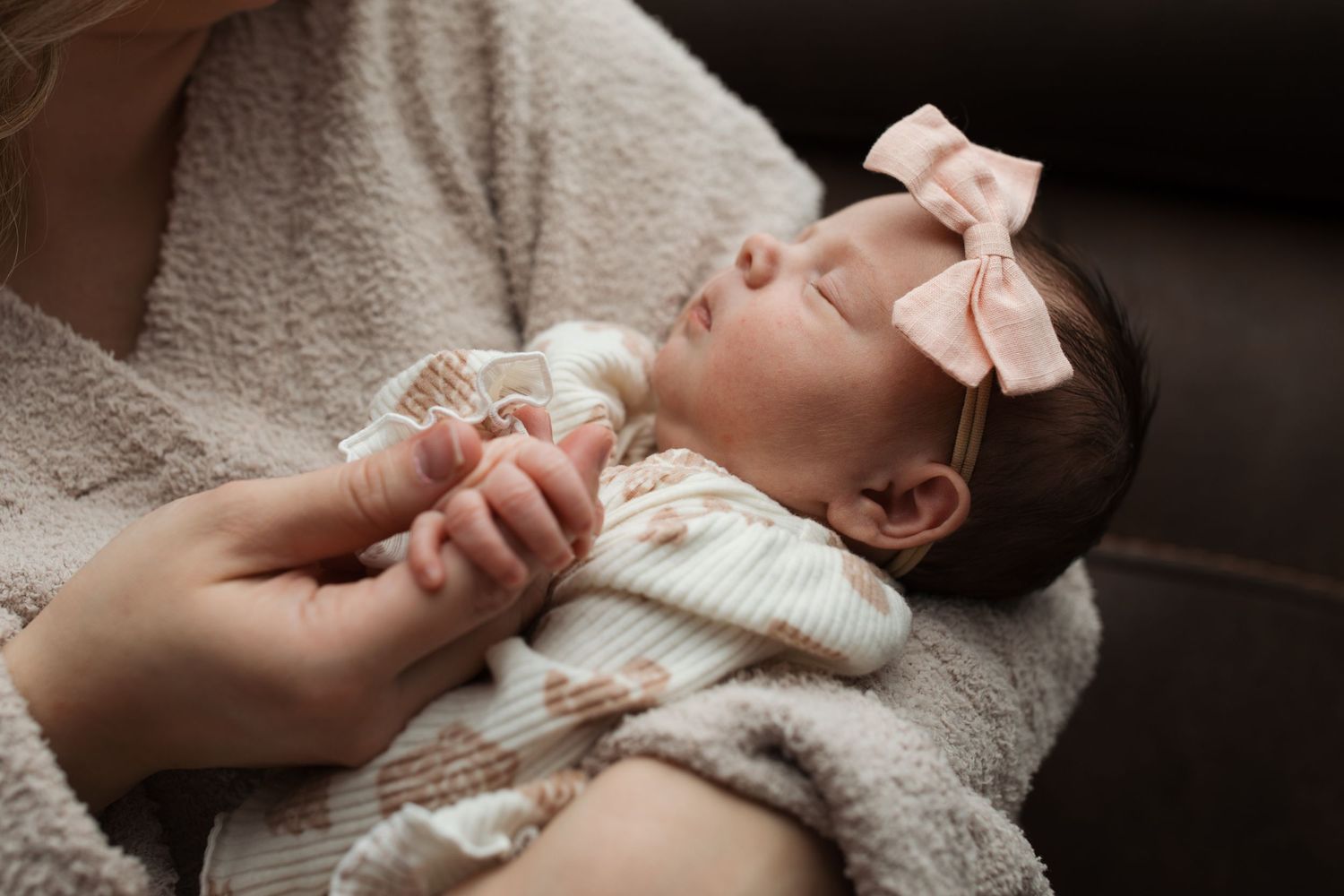 Newborn baby girl resting in her mother’s arms, holding her mom’s hand during a cozy lifestyle session in Middleton, Idaho.
