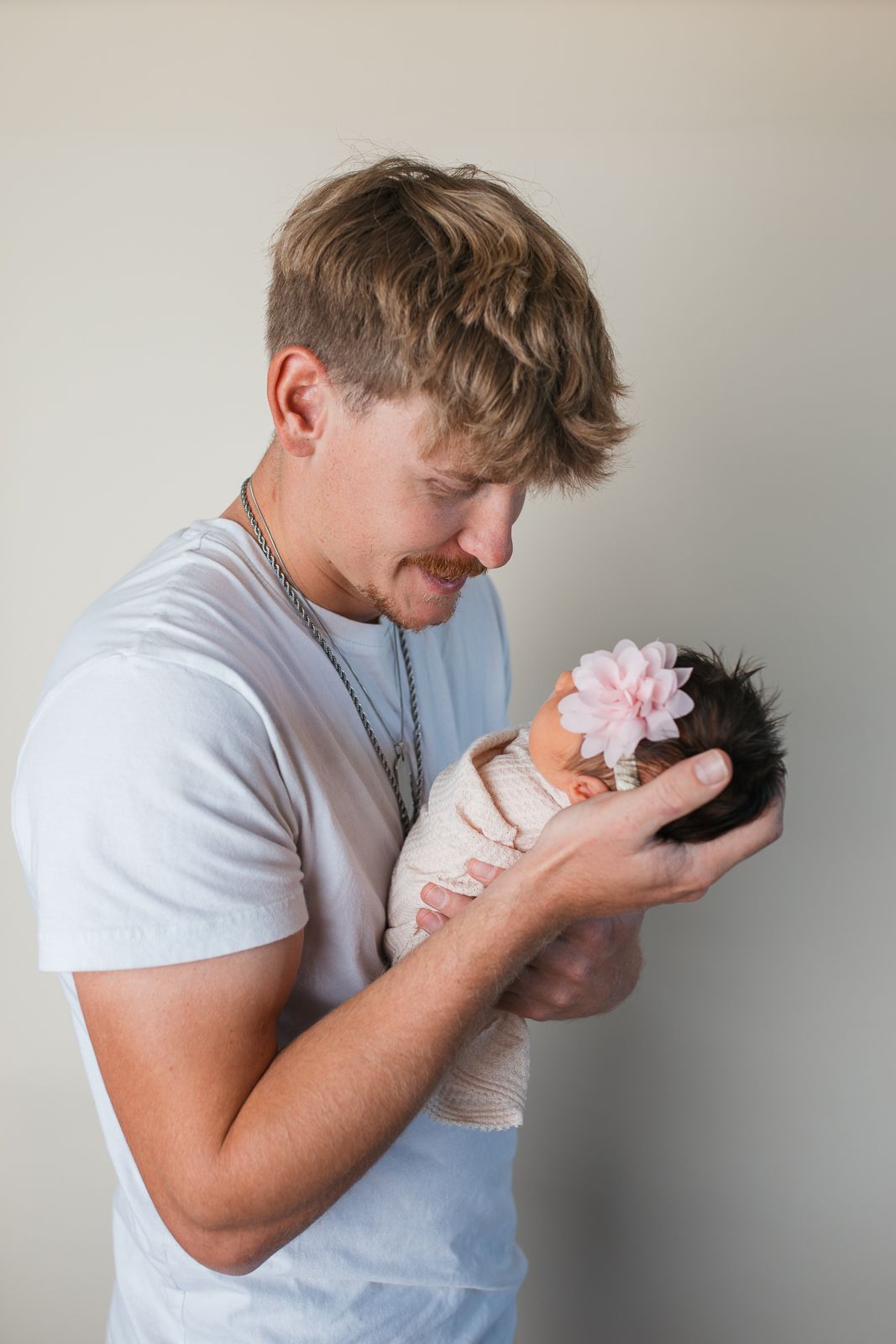 Four sequential photos show tender moments of a person in a light shirt holding and gently kissing a small baby studio newborn photography