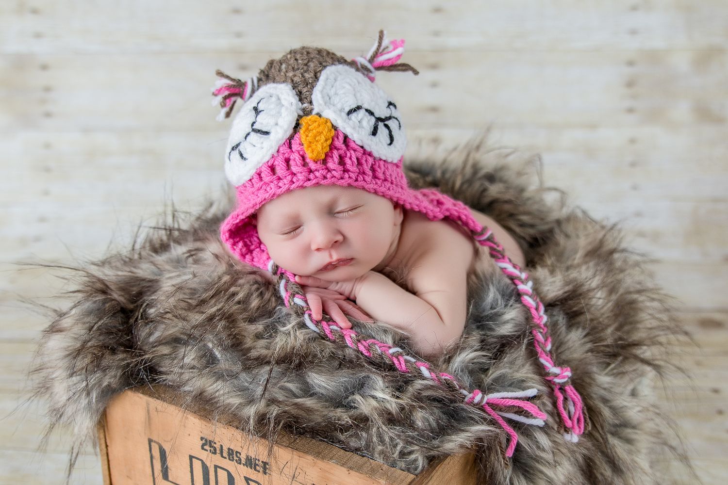Sleeping baby wearing pink knit hat rests peacefully on soft gray fur blanket -studio newborn photography Caldwell Idaho
