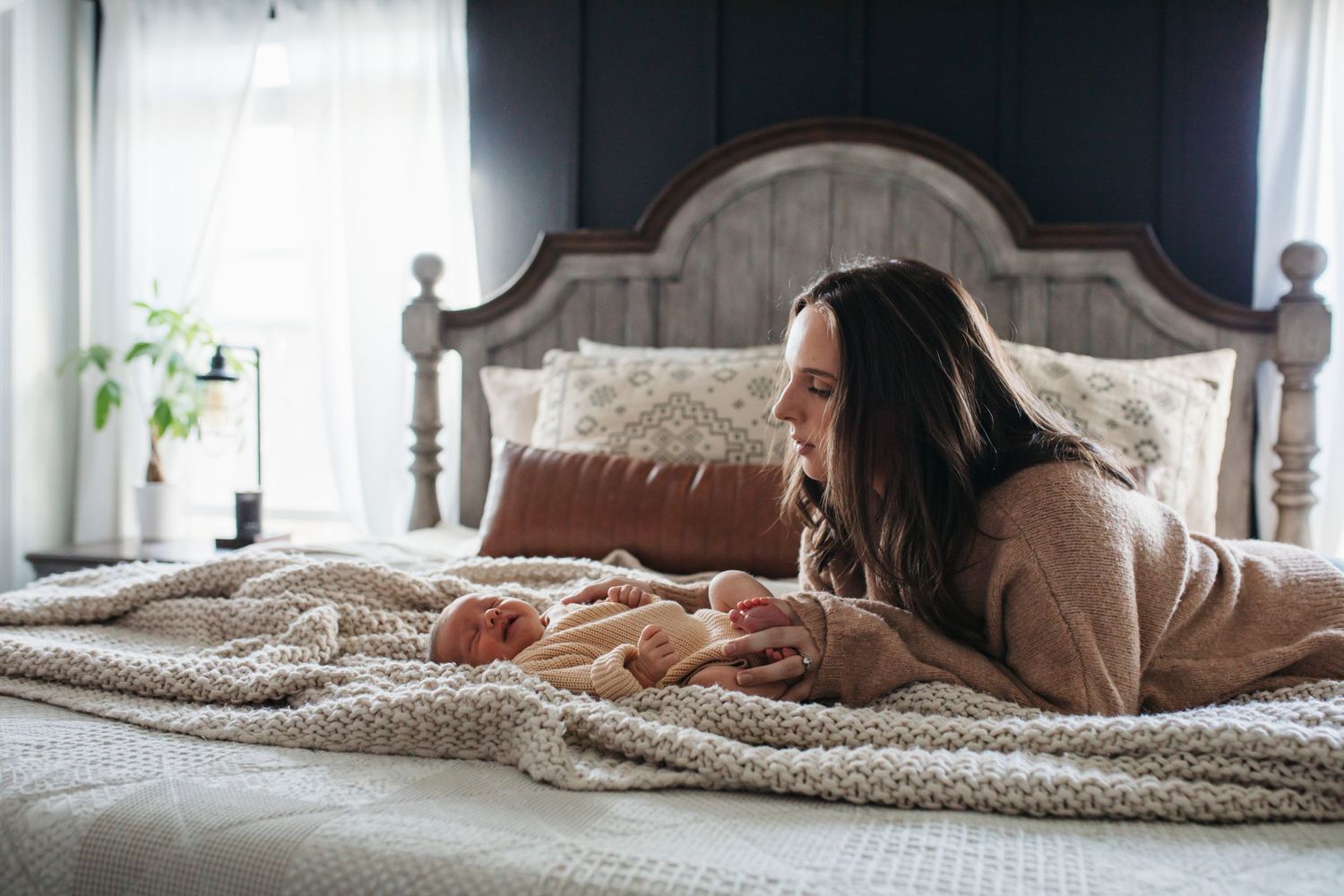 Woman lying on white bedding while relaxing at home during a cozy morning with her baby - lifestyle in-home newborn photos Boise