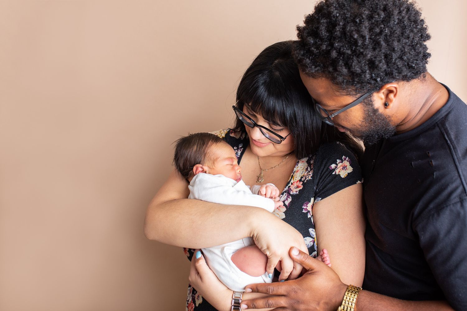 Parents lovingly embrace their newborn baby against a neutral beige background studio newborn photography Nampa Idaho