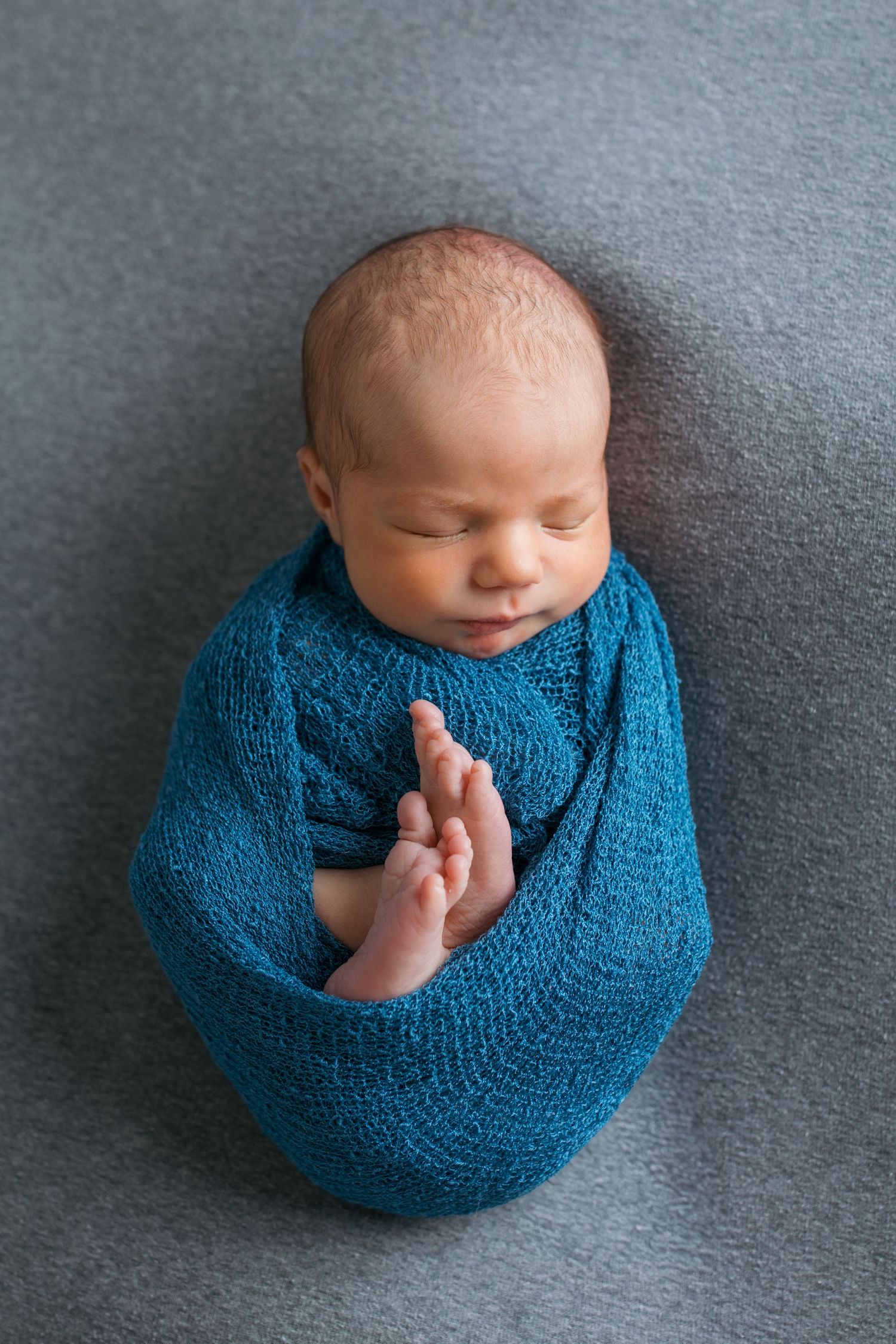 Overhead studio portrait of newborn baby boy wrapped in blue swaddle on soft gray blanket