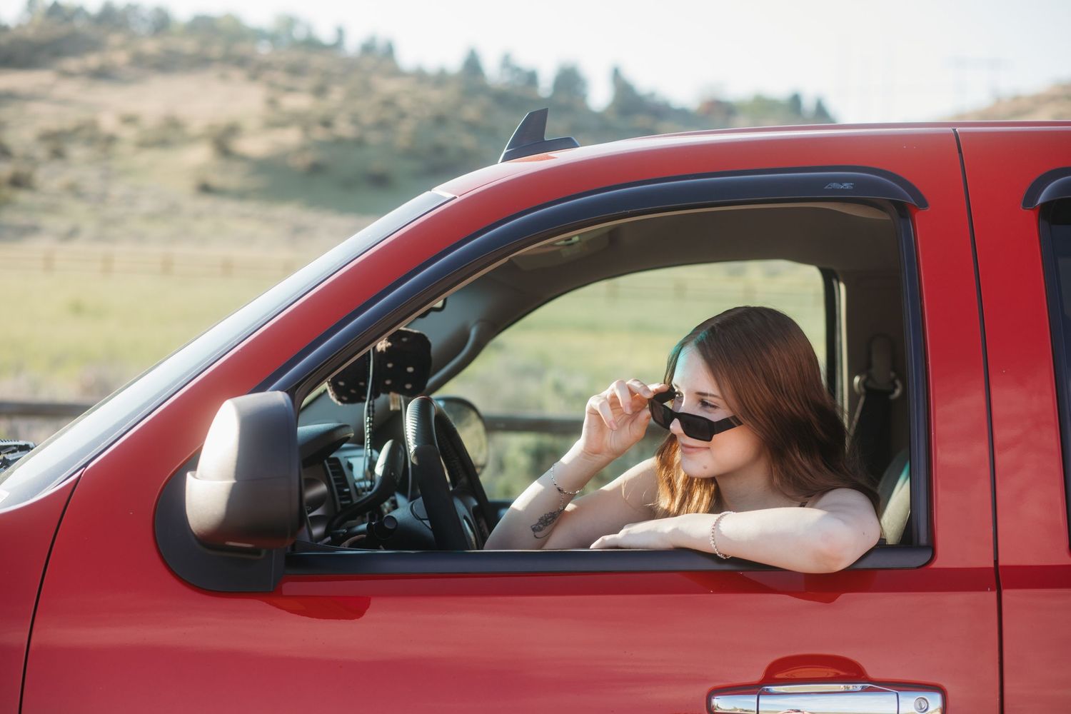 Boise senior photos of high school girl wearing sunglasses sitting in red truck during outdoor golden hour session