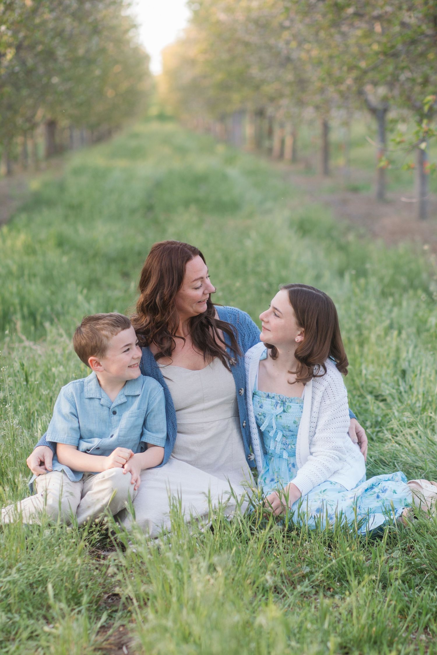 Mom and kids smiling at each other in blossom orchard during golden hour spring session in Caldwell Idaho