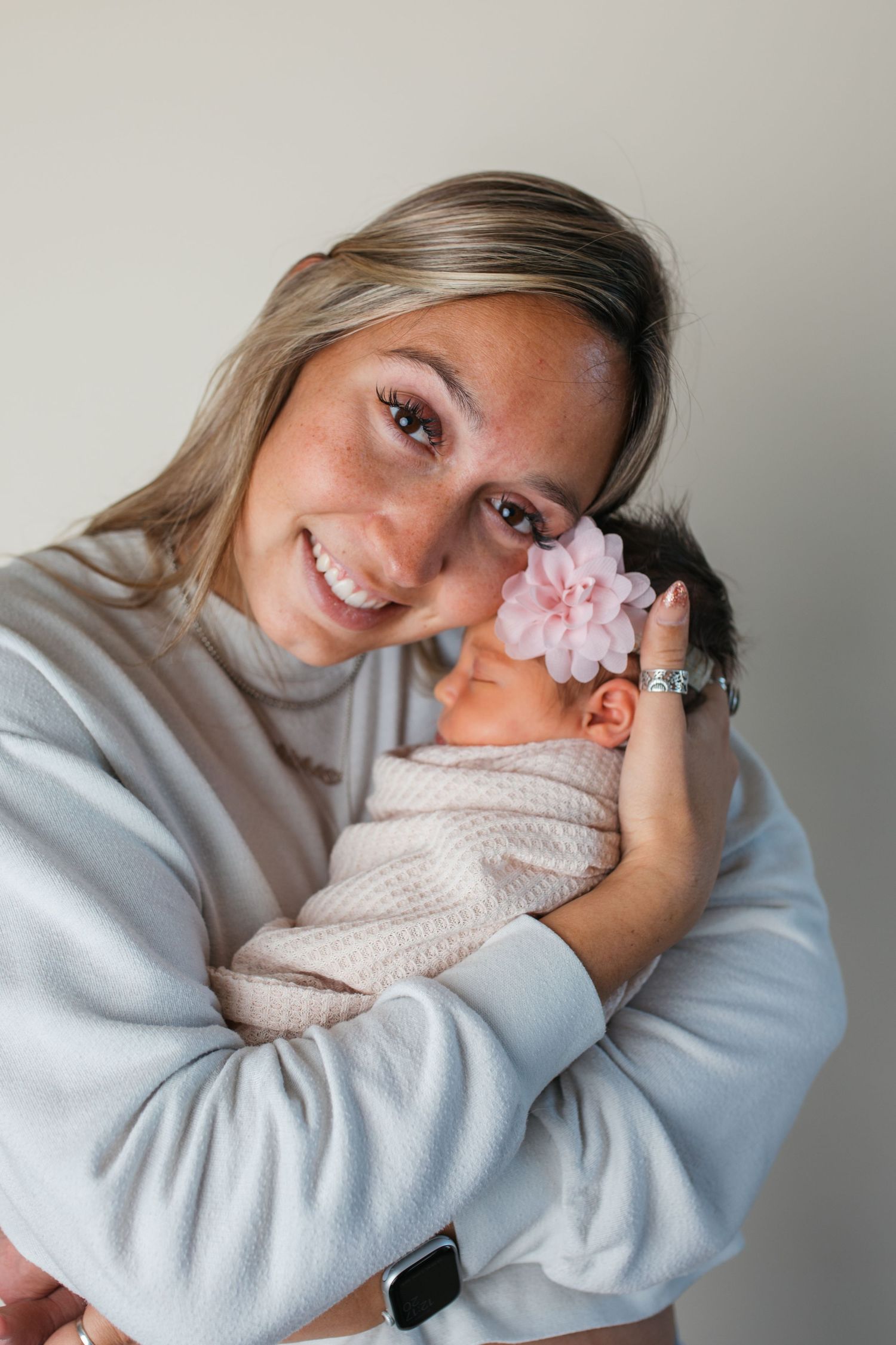 Caldwell Idaho newborn photographer portrait of a mother holding her swaddled newborn baby with a pink floral headband.