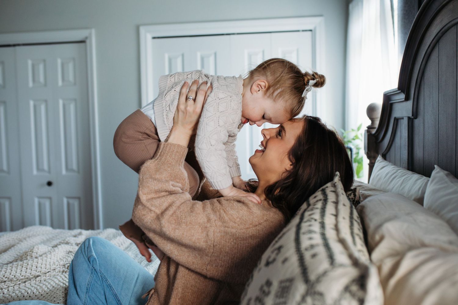 A tender moment shared between parent and baby while relaxing together on a cozy bed with white bedding -in-home lifestyle family photos