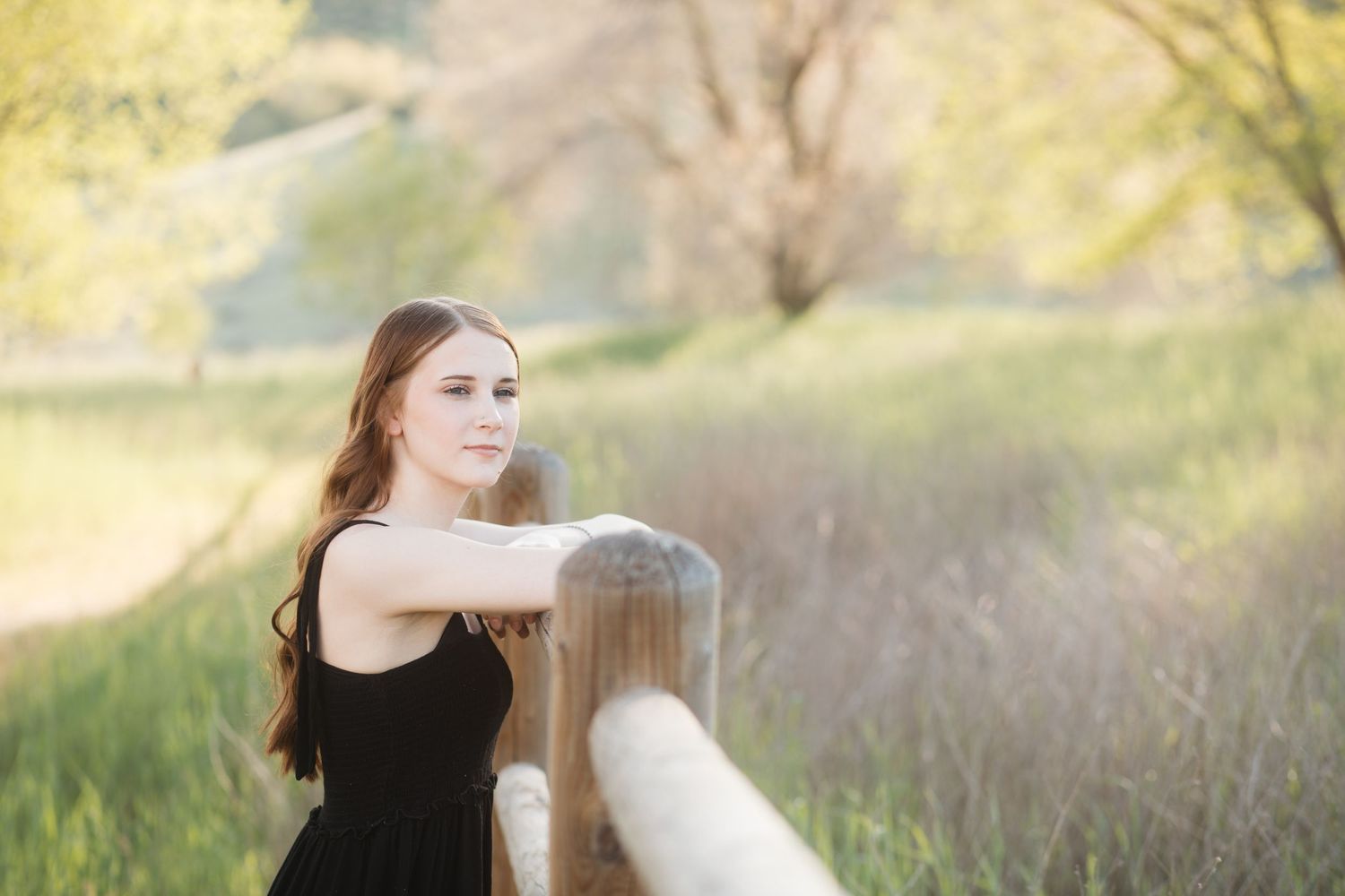Boise senior photos of high school girl leaning on wooden fence in soft golden hour light looking off into distance